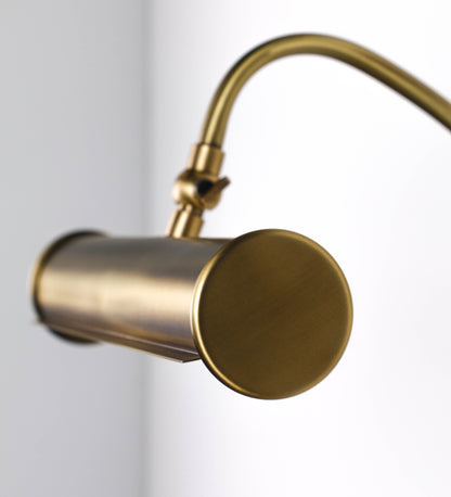 Aplique de parede que combina elementos clássicos com toques contemporâneos, todo em ouro velho. O aplique é composto por uma base circular de onde se estende um braço curvo e gracioso, que suporta a barra principal. O braço contém um elemento que permite apertar ou desapertar a barra para melhor manipular a direção da luz. A barra de 25cm de largura é cilíndrica e alongada. As extremidades do cilindro são planas e do mesmo diâmetro.