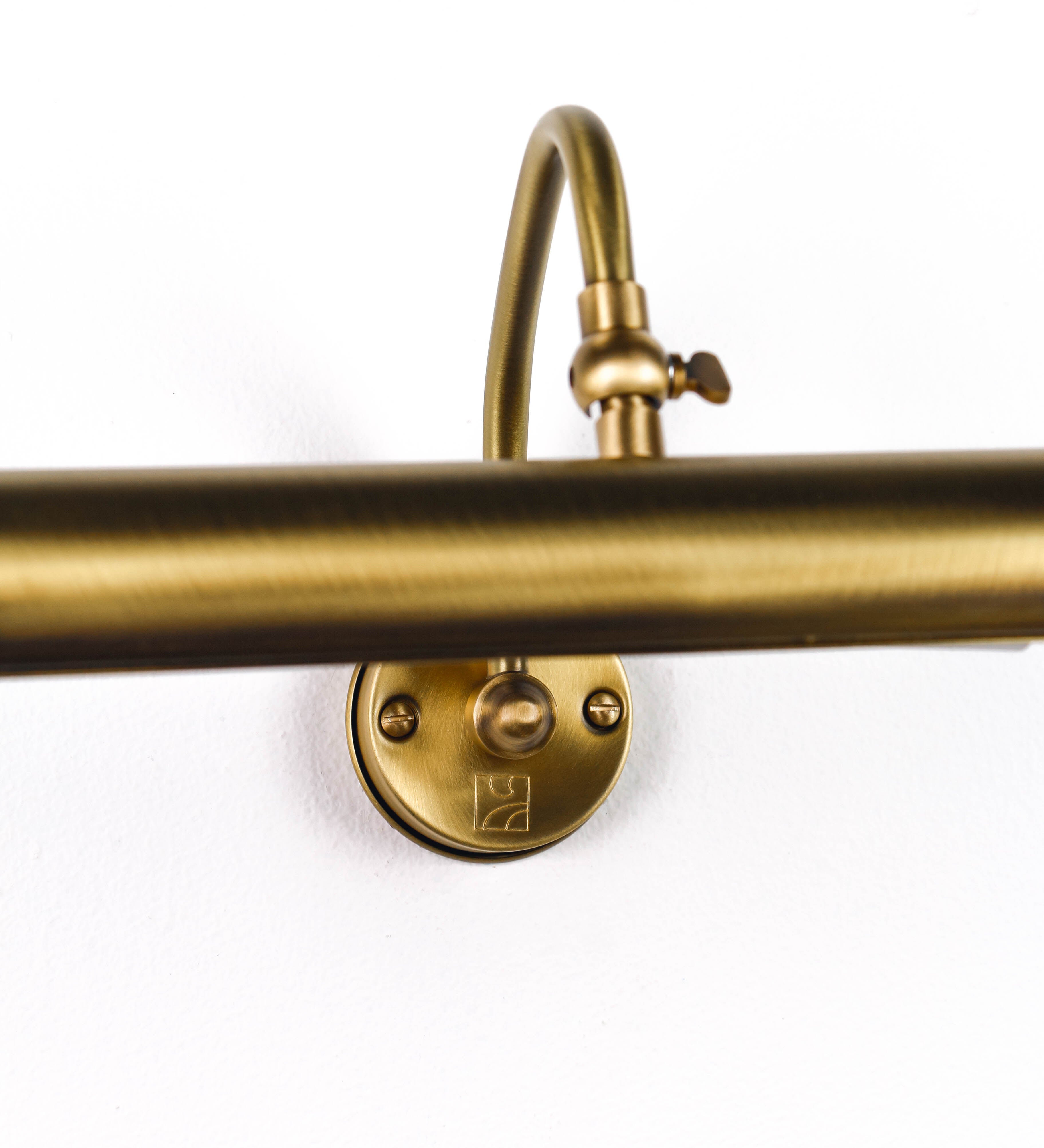 Aplique de parede que combina elementos clássicos com toques contemporâneos, todo em ouro velho. O aplique é composto por uma base circular de onde se estende um braço curvo e gracioso, que suporta a barra principal. O braço contém um elemento que permite apertar ou desapertar a barra para melhor manipular a direção da luz. A barra de 25cm de largura é cilíndrica e alongada. As extremidades do cilindro são planas e do mesmo diâmetro.