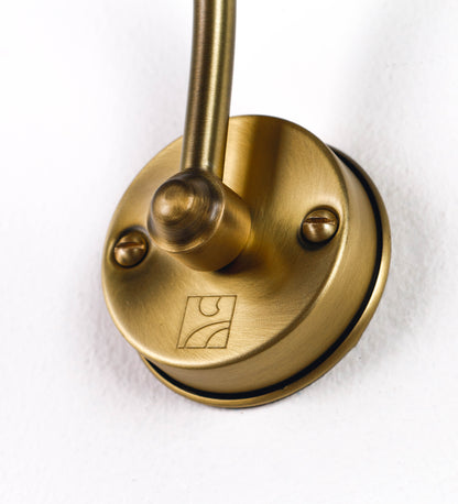 Aplique de parede que combina elementos clássicos com toques contemporâneos, todo em ouro velho. O aplique é composto por uma base circular de onde se estende um braço curvo e gracioso, que suporta a barra principal. O braço contém um elemento que permite apertar ou desapertar a barra para melhor manipular a direção da luz. A barra de 25cm de largura é cilíndrica e alongada. As extremidades do cilindro são planas e do mesmo diâmetro.