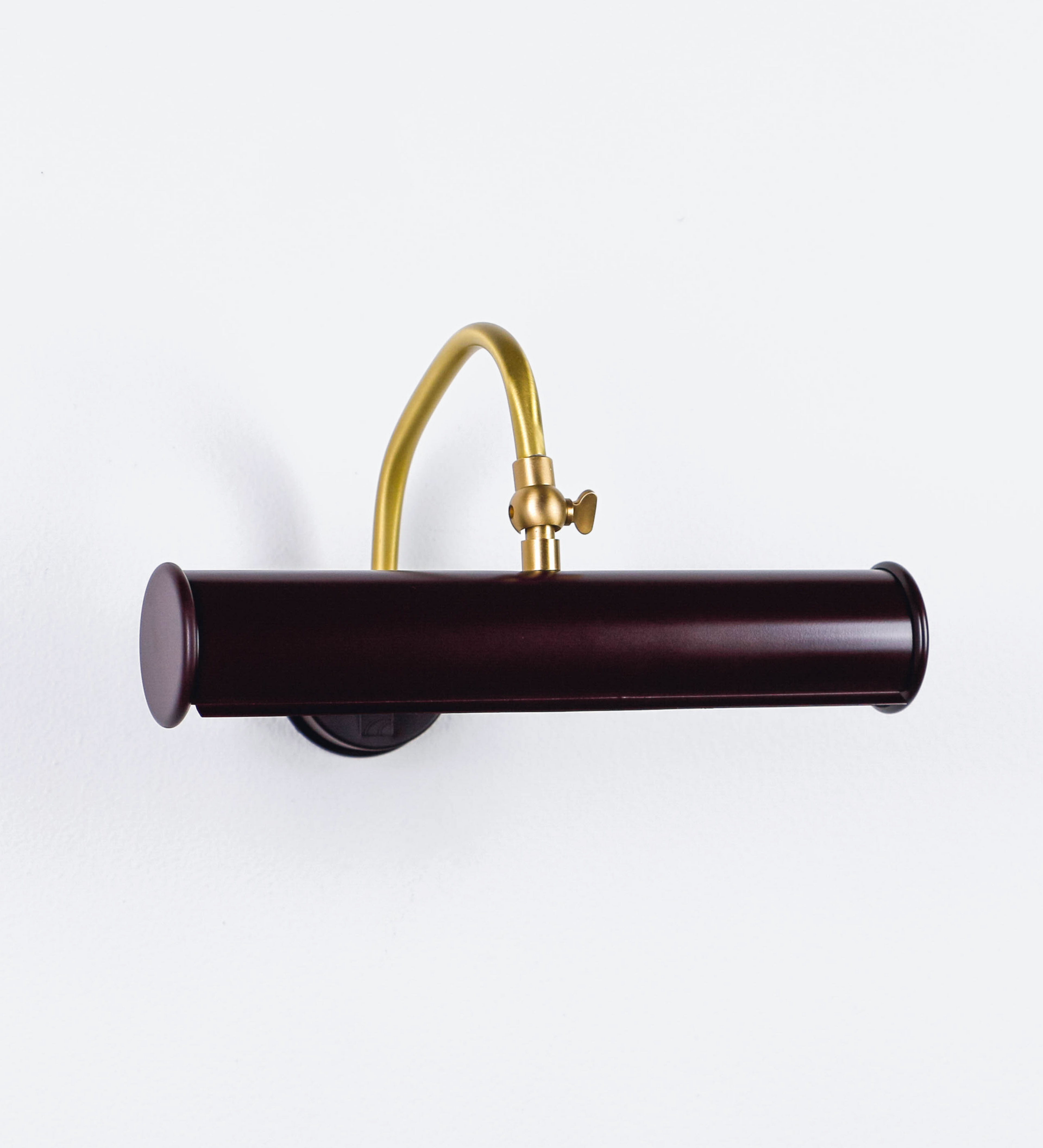 Aplique de parede que combina elementos clássicos com toques contemporâneos. O aplique é composto por uma base circular tom vinho, de onde se estende um braço curvo e gracioso, em latão escovado, que suporta a barra principal. O braço contém um elemento, em latão escovado, que permite apertar ou desapertar a barra para melhor manipular a direção da luz. A barra de 25cm de largura, é cilíndrica e alongada, tom vinho. As extremidades do cilindro são planas e do mesmo diâmetro.
