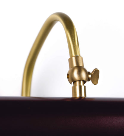 Aplique de parede que combina elementos clássicos com toques contemporâneos. O aplique é composto por uma base circular tom vinho, de onde se estende um braço curvo e gracioso, em latão escovado, que suporta a barra principal. O braço contém um elemento, em latão escovado, que permite apertar ou desapertar a barra para melhor manipular a direção da luz. A barra de 25cm de largura, é cilíndrica e alongada, tom vinho. As extremidades do cilindro são planas e do mesmo diâmetro.