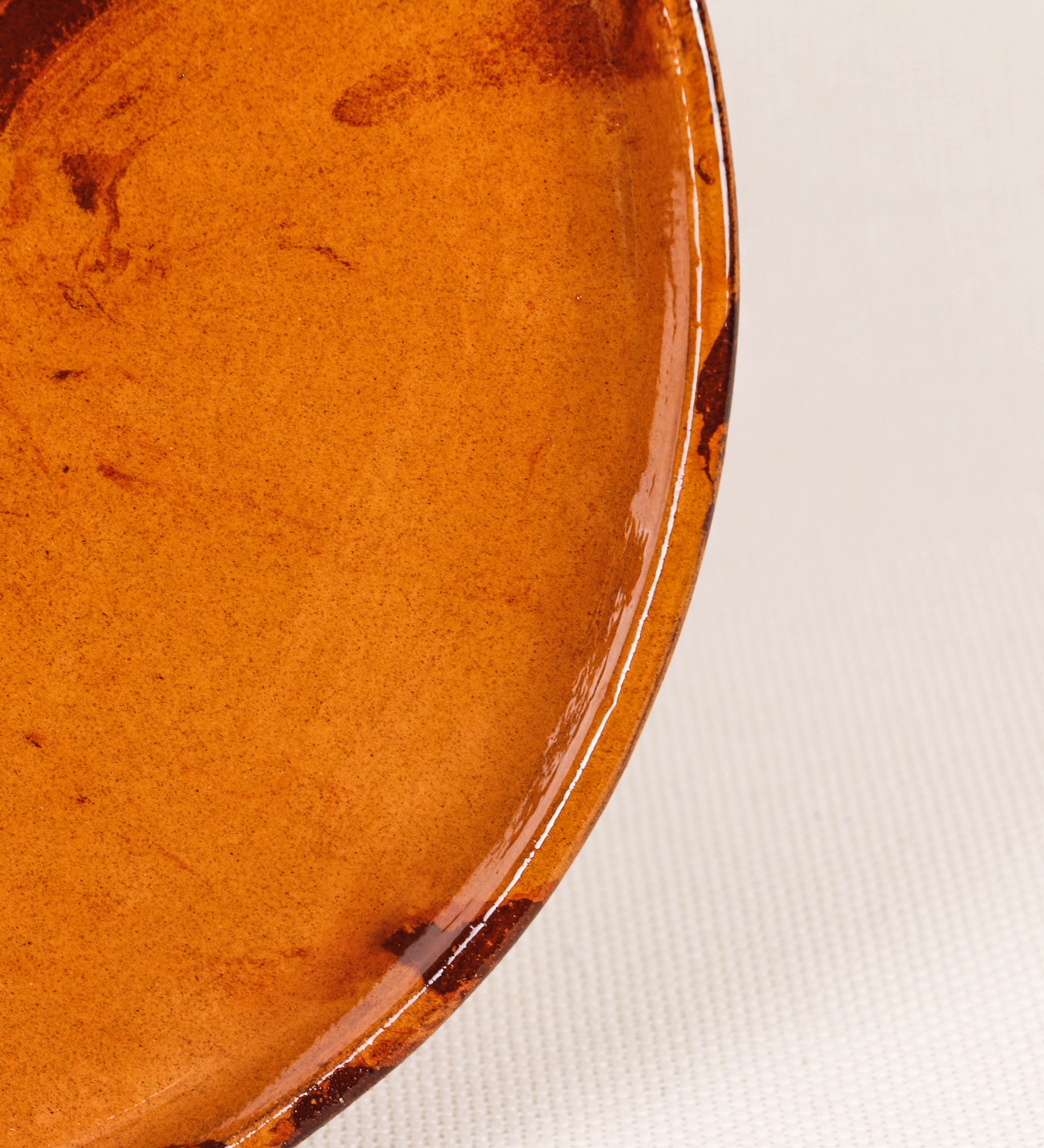 Prato raso com design minimalista e distinto. O prato é de barro, com uma mistura de dois tipos de barro diferentes, um mais escuro e outro mais claro. Esta mistura cria um desenho de formas abstratas e aleatórias, que se espalham por todas as superfícies do prato. Tem acabamento vidrado castanho translúcido, escurecendo as cores originais dos barros misturados. A forma do prato é circular, com uma borda envolvente de altura baixa e design simples e minimalista. 