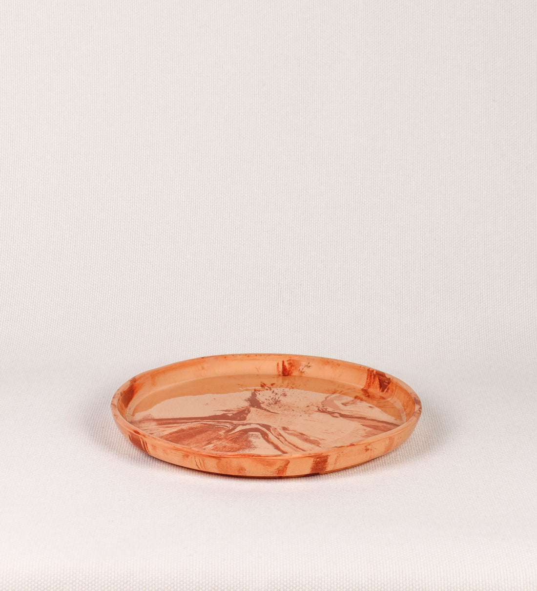 Prato raso com design minimalista e distinto. O prato é de barro, com uma mistura dois tipos de barro diferentes, um mais escuro e outro mais claro. Esta mistura cria um desenho de formas abstratas e aleatórias, que se espalham por todas as superfícies do prato. Tem um acabamento vidrado transparente com brilho, conferindo um toque de sofisticação e preservando os tons naturais dos barros. A forma do prato é circular, com uma borda envolvente de altura baixa e design simples e minimalista. 