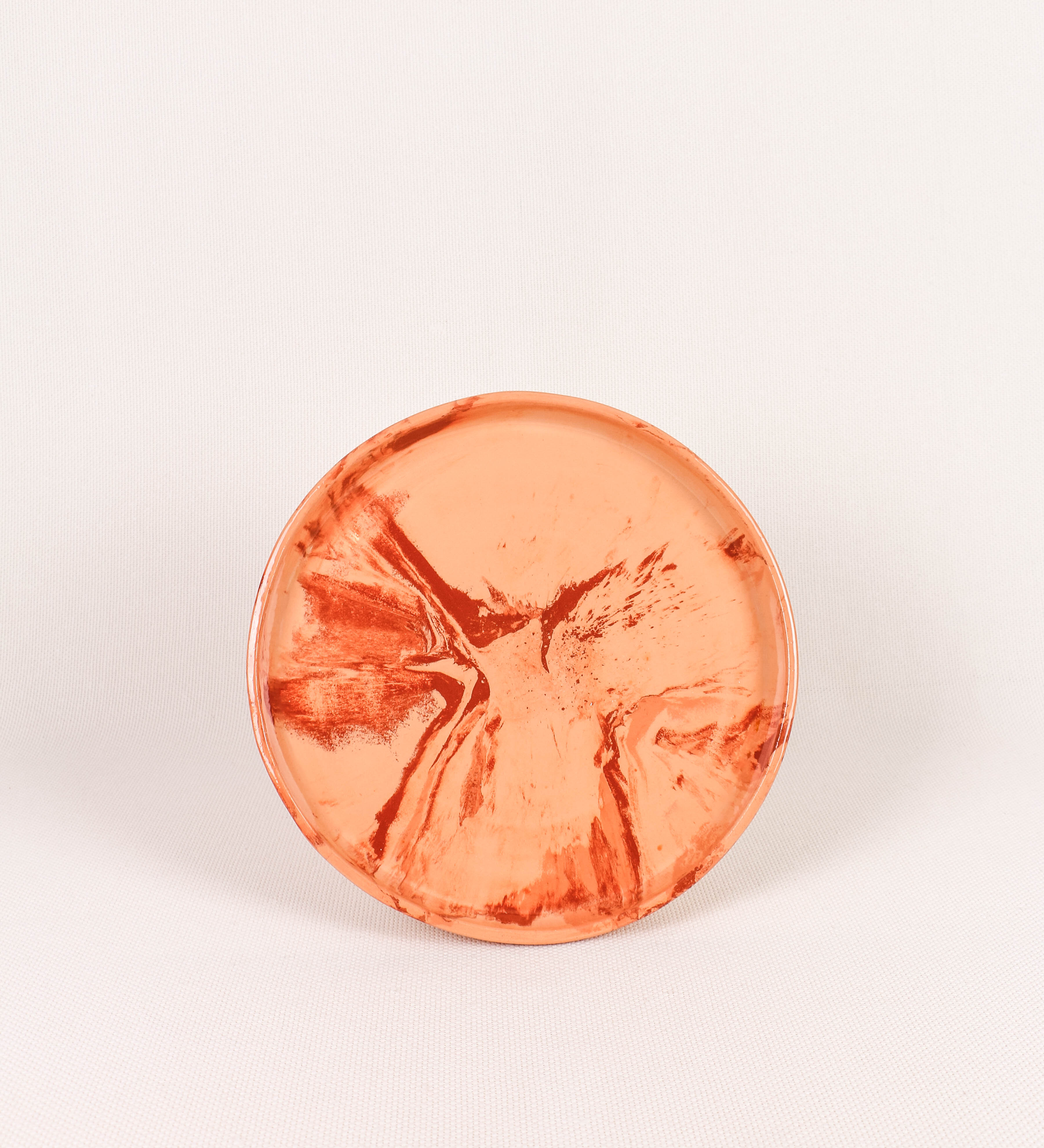Prato raso com design minimalista e distinto. O prato é de barro, com uma mistura dois tipos de barro diferentes, um mais escuro e outro mais claro. Esta mistura cria um desenho de formas abstratas e aleatórias, que se espalham por todas as superfícies do prato. Tem um acabamento vidrado transparente com brilho, conferindo um toque de sofisticação e preservando os tons naturais dos barros. A forma do prato é circular, com uma borda envolvente de altura baixa e design simples e minimalista. 
