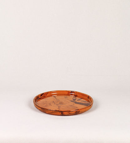 Prato de aperitivos com design minimalista e distinto. O prato é de barro, com uma mistura de dois tipos de barro diferentes, um mais escuro e outro mais claro. Esta mistura cria um desenho de formas abstratas e aleatórias, que se espalham por todas as superfícies do prato. Tem acabamento vidrado castanho translúcido, escurecendo as cores originais dos barros misturados. A forma do prato é circular, com uma borda envolvente de altura baixa e design simples e minimalista. 