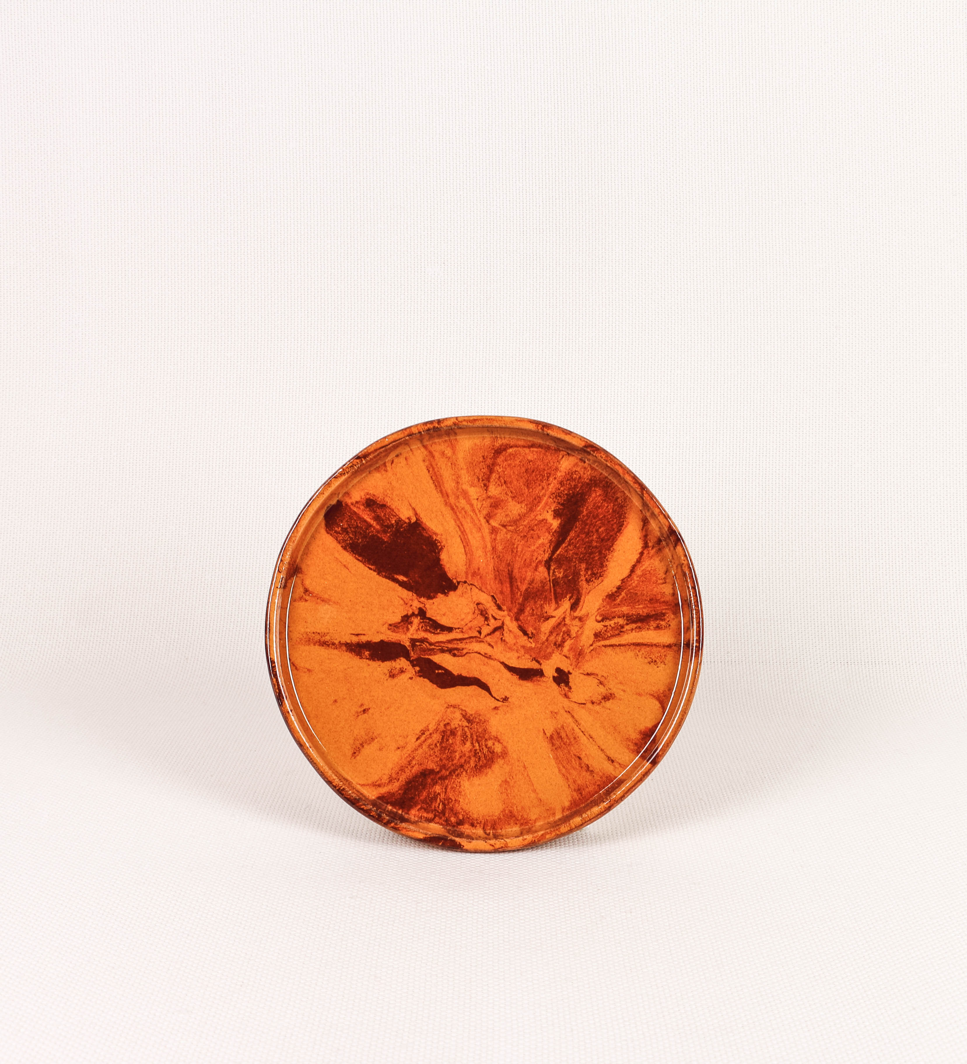 Prato de aperitivos com design minimalista e distinto. O prato é de barro, com uma mistura de dois tipos de barro diferentes, um mais escuro e outro mais claro. Esta mistura cria um desenho de formas abstratas e aleatórias, que se espalham por todas as superfícies do prato. Tem acabamento vidrado castanho translúcido, escurecendo as cores originais dos barros misturados. A forma do prato é circular, com uma borda envolvente de altura baixa e design simples e minimalista. 