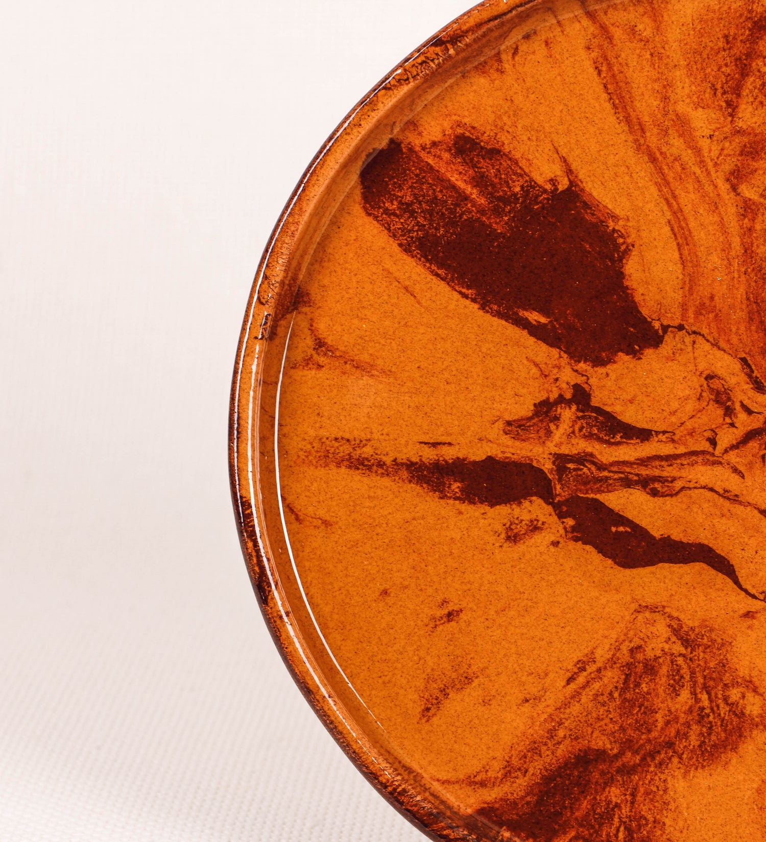 Prato de aperitivos com design minimalista e distinto. O prato é de barro, com uma mistura de dois tipos de barro diferentes, um mais escuro e outro mais claro. Esta mistura cria um desenho de formas abstratas e aleatórias, que se espalham por todas as superfícies do prato. Tem acabamento vidrado castanho translúcido, escurecendo as cores originais dos barros misturados. A forma do prato é circular, com uma borda envolvente de altura baixa e design simples e minimalista. 