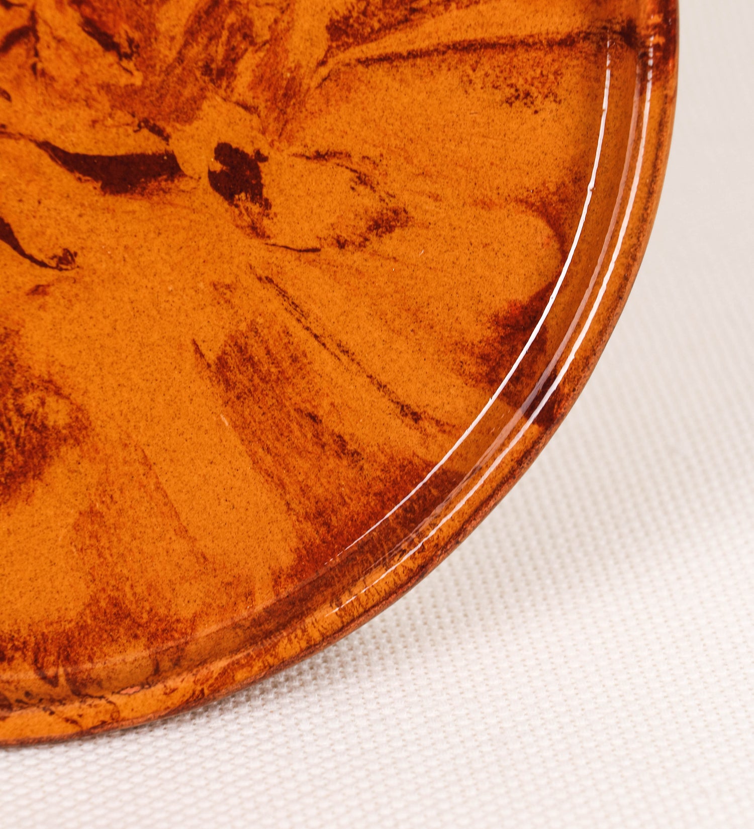 Prato de aperitivos com design minimalista e distinto. O prato é de barro, com uma mistura de dois tipos de barro diferentes, um mais escuro e outro mais claro. Esta mistura cria um desenho de formas abstratas e aleatórias, que se espalham por todas as superfícies do prato. Tem acabamento vidrado castanho translúcido, escurecendo as cores originais dos barros misturados. A forma do prato é circular, com uma borda envolvente de altura baixa e design simples e minimalista. 
