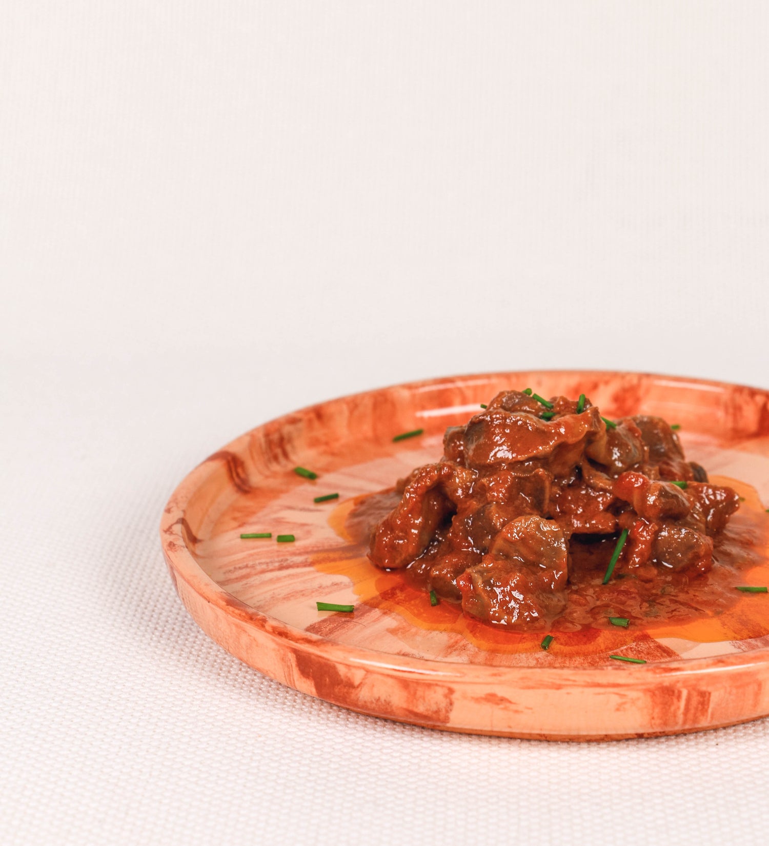Prato de aperitivos com design minimalista e distinto. O prato é de barro, com uma mistura dois tipos de barro diferentes, um mais escuro e outro mais claro. Esta mistura cria um desenho de formas abstratas e aleatórias, que se espalham por todas as superfícies do prato. Tem um acabamento vidrado transparente com brilho, conferindo um toque de sofisticação e preservando os tons naturais dos barros. A forma do prato é circular, com uma borda envolvente de altura baixa e design simples e minimalista. 