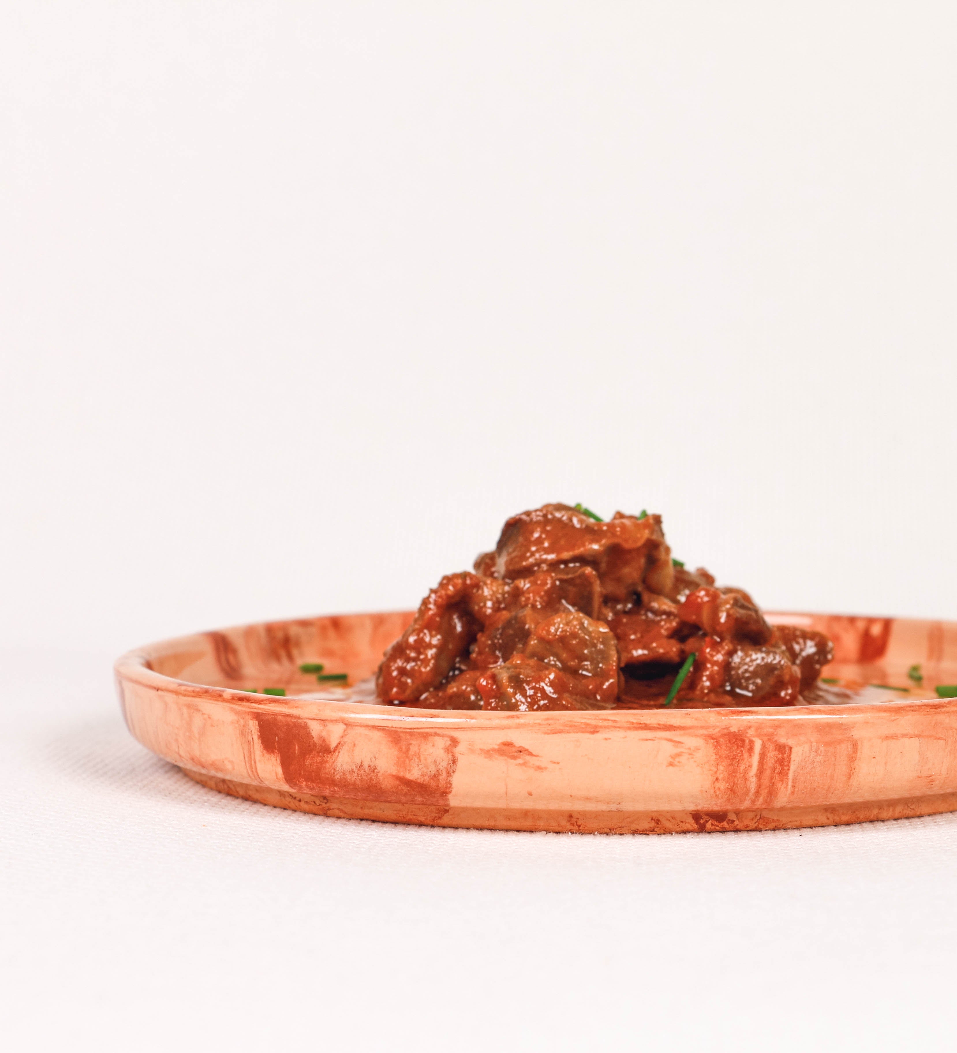 Prato de aperitivos com design minimalista e distinto. O prato é de barro, com uma mistura dois tipos de barro diferentes, um mais escuro e outro mais claro. Esta mistura cria um desenho de formas abstratas e aleatórias, que se espalham por todas as superfícies do prato. Tem um acabamento vidrado transparente com brilho, conferindo um toque de sofisticação e preservando os tons naturais dos barros. A forma do prato é circular, com uma borda envolvente de altura baixa e design simples e minimalista. 