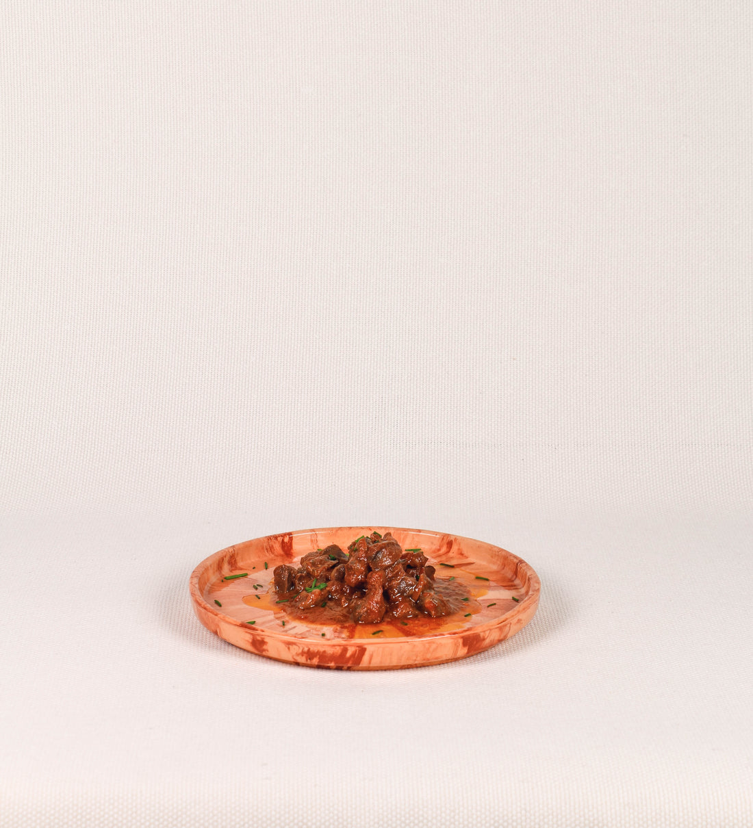Prato de aperitivos com design minimalista e distinto. O prato é de barro, com uma mistura dois tipos de barro diferentes, um mais escuro e outro mais claro. Esta mistura cria um desenho de formas abstratas e aleatórias, que se espalham por todas as superfícies do prato. Tem um acabamento vidrado transparente com brilho, conferindo um toque de sofisticação e preservando os tons naturais dos barros. A forma do prato é circular, com uma borda envolvente de altura baixa e design simples e minimalista. 