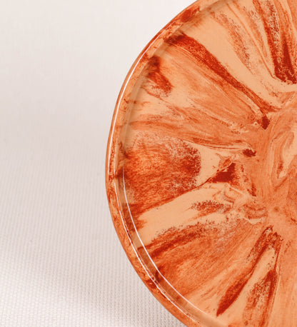 Prato de aperitivos com design minimalista e distinto. O prato é de barro, com uma mistura dois tipos de barro diferentes, um mais escuro e outro mais claro. Esta mistura cria um desenho de formas abstratas e aleatórias, que se espalham por todas as superfícies do prato. Tem um acabamento vidrado transparente com brilho, conferindo um toque de sofisticação e preservando os tons naturais dos barros. A forma do prato é circular, com uma borda envolvente de altura baixa e design simples e minimalista. 