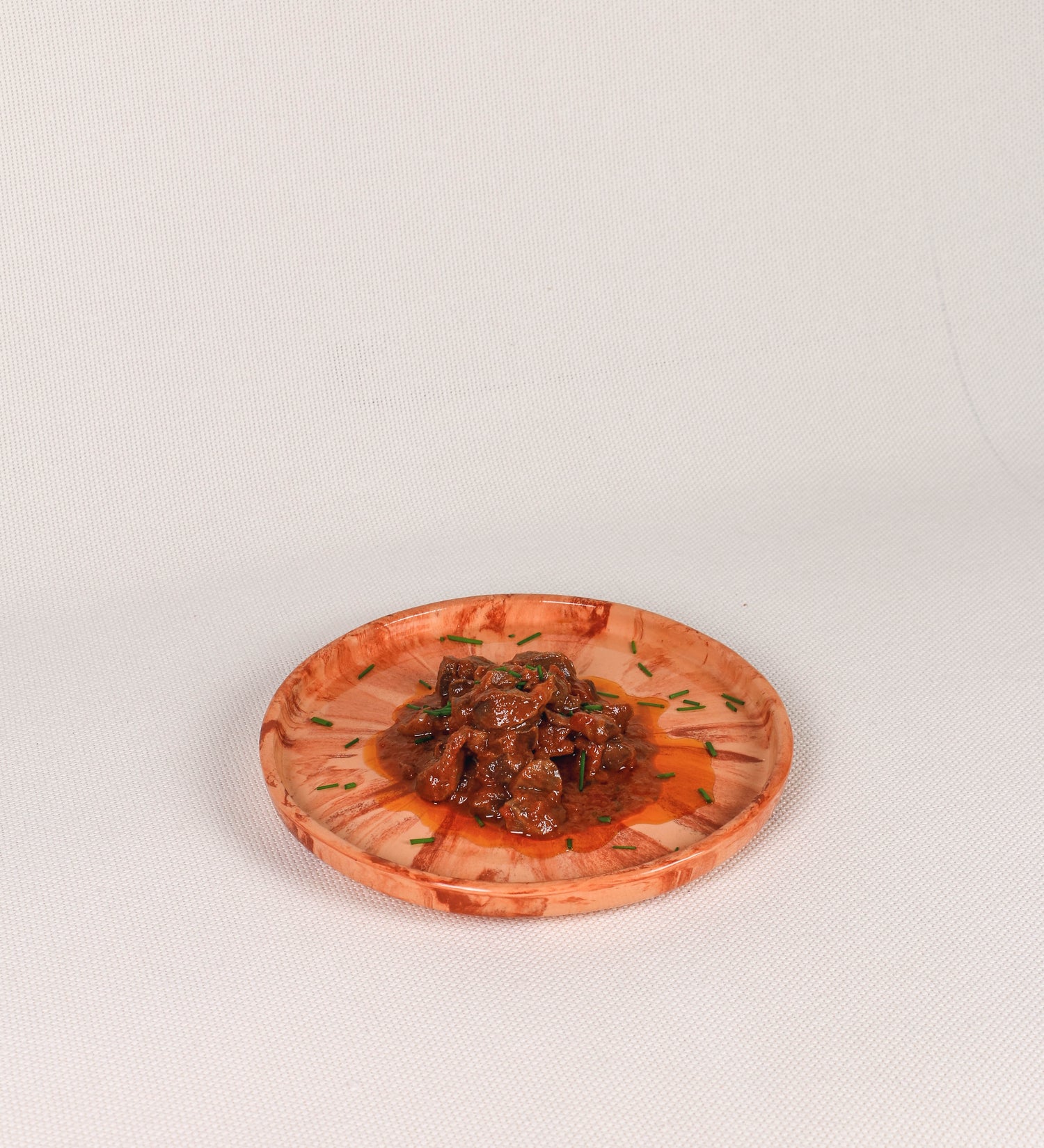 Prato de aperitivos com design minimalista e distinto. O prato é de barro, com uma mistura dois tipos de barro diferentes, um mais escuro e outro mais claro. Esta mistura cria um desenho de formas abstratas e aleatórias, que se espalham por todas as superfícies do prato. Tem um acabamento vidrado transparente com brilho, conferindo um toque de sofisticação e preservando os tons naturais dos barros. A forma do prato é circular, com uma borda envolvente de altura baixa e design simples e minimalista. 