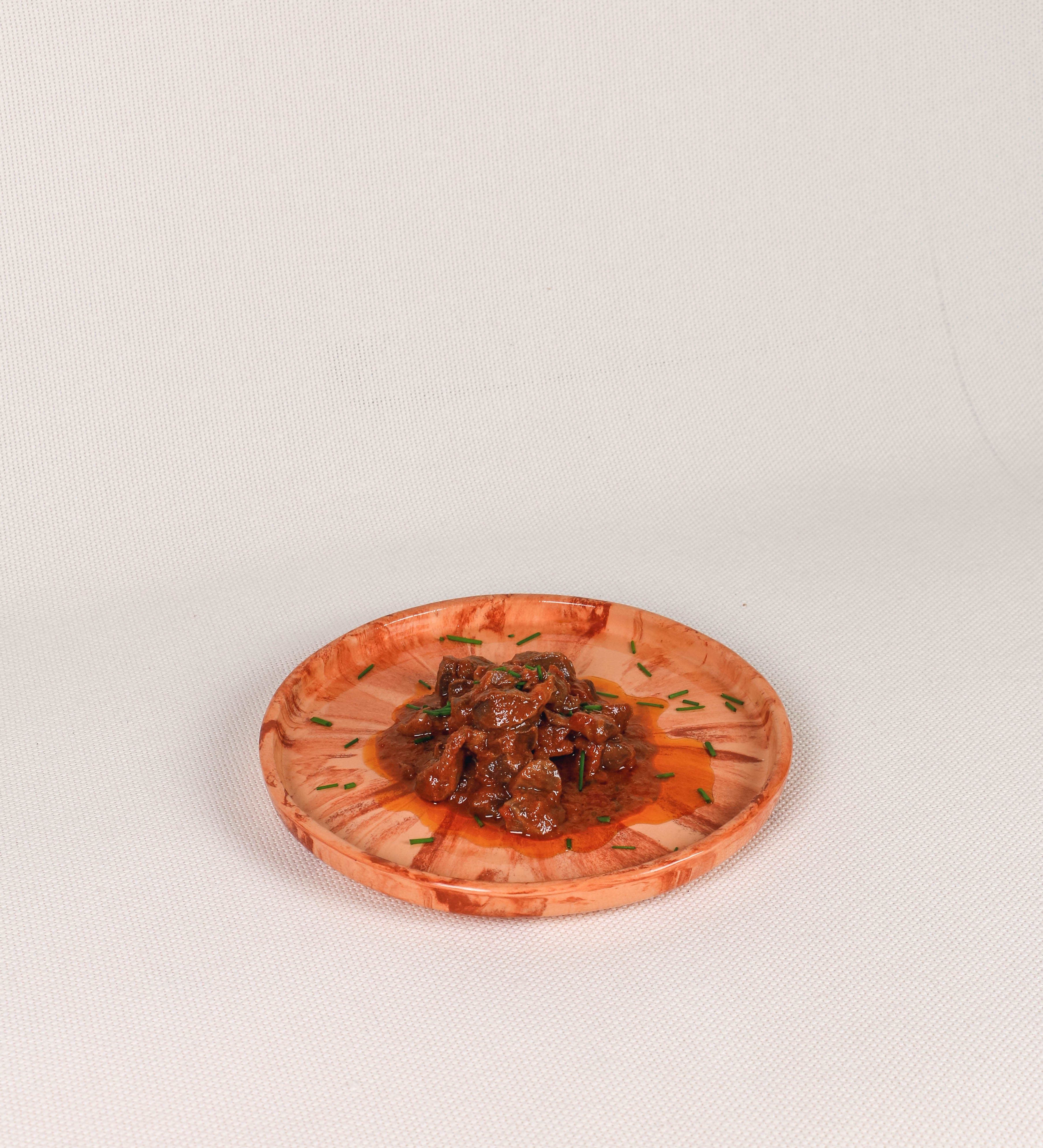 Prato de aperitivos com design minimalista e distinto. O prato é de barro, com uma mistura dois tipos de barro diferentes, um mais escuro e outro mais claro. Esta mistura cria um desenho de formas abstratas e aleatórias, que se espalham por todas as superfícies do prato. Tem um acabamento vidrado transparente com brilho, conferindo um toque de sofisticação e preservando os tons naturais dos barros. A forma do prato é circular, com uma borda envolvente de altura baixa e design simples e minimalista. 