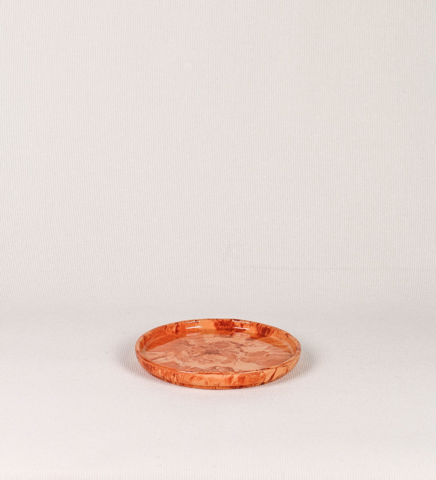 Prato de sobremesa com design minimalista e distinto. O prato é de barro, com uma mistura dois tipos de barro diferentes, um mais escuro e outro mais claro. Esta mistura cria um desenho de formas abstratas e aleatórias, que se espalham por todas as superfícies do prato. Tem um acabamento vidrado transparente com brilho, conferindo um toque de sofisticação e preservando os tons naturais dos barros. A forma do prato é circular, com uma borda envolvente de altura baixa e design simples e minimalista. 