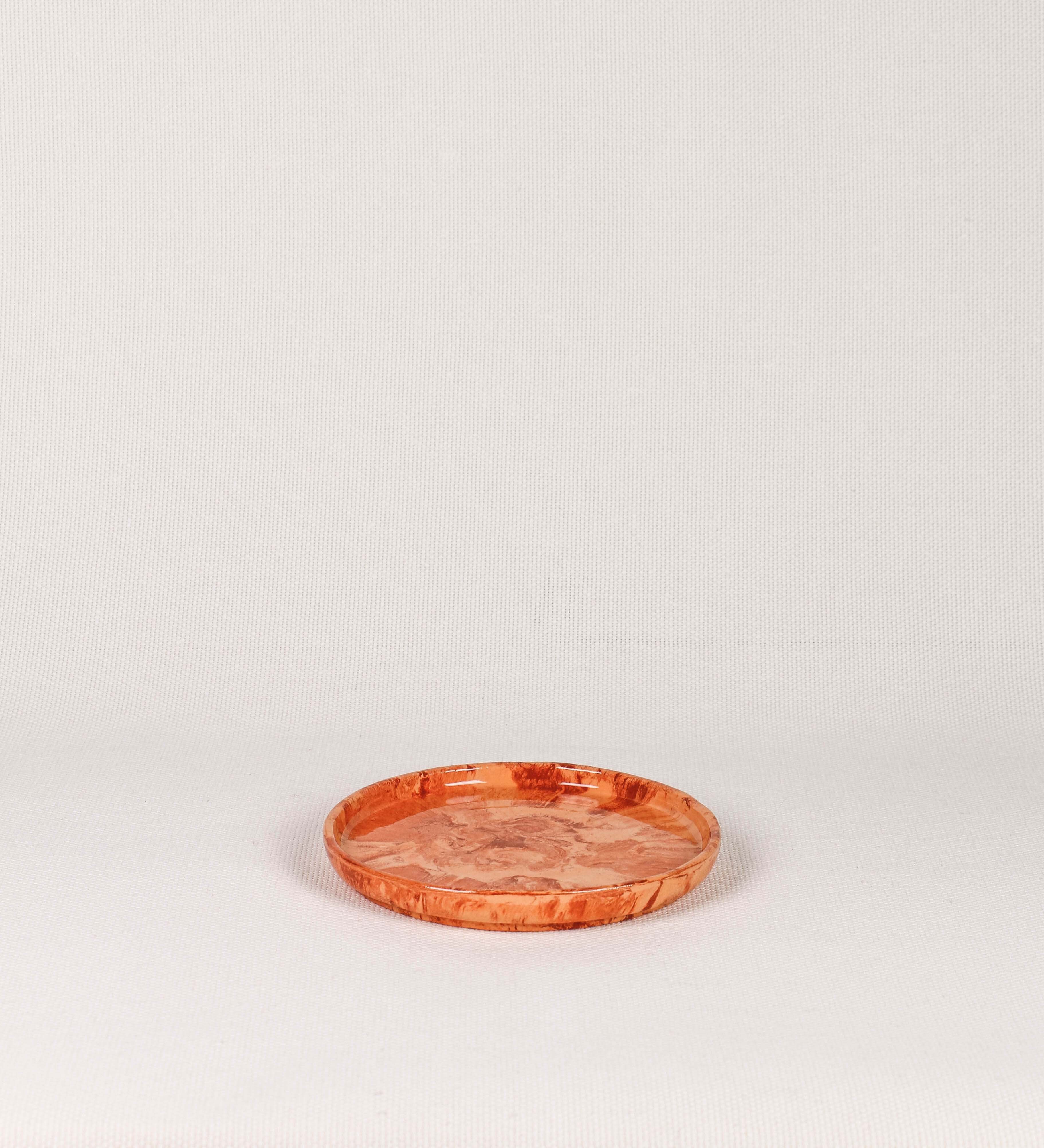 Prato de sobremesa com design minimalista e distinto. O prato é de barro, com uma mistura dois tipos de barro diferentes, um mais escuro e outro mais claro. Esta mistura cria um desenho de formas abstratas e aleatórias, que se espalham por todas as superfícies do prato. Tem um acabamento vidrado transparente com brilho, conferindo um toque de sofisticação e preservando os tons naturais dos barros. A forma do prato é circular, com uma borda envolvente de altura baixa e design simples e minimalista. 