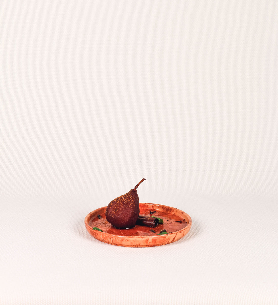 Prato de sobremesa com design minimalista e distinto. O prato é de barro, com uma mistura dois tipos de barro diferentes, um mais escuro e outro mais claro. Esta mistura cria um desenho de formas abstratas e aleatórias, que se espalham por todas as superfícies do prato. Tem um acabamento vidrado transparente com brilho, conferindo um toque de sofisticação e preservando os tons naturais dos barros. A forma do prato é circular, com uma borda envolvente de altura baixa e design simples e minimalista. 