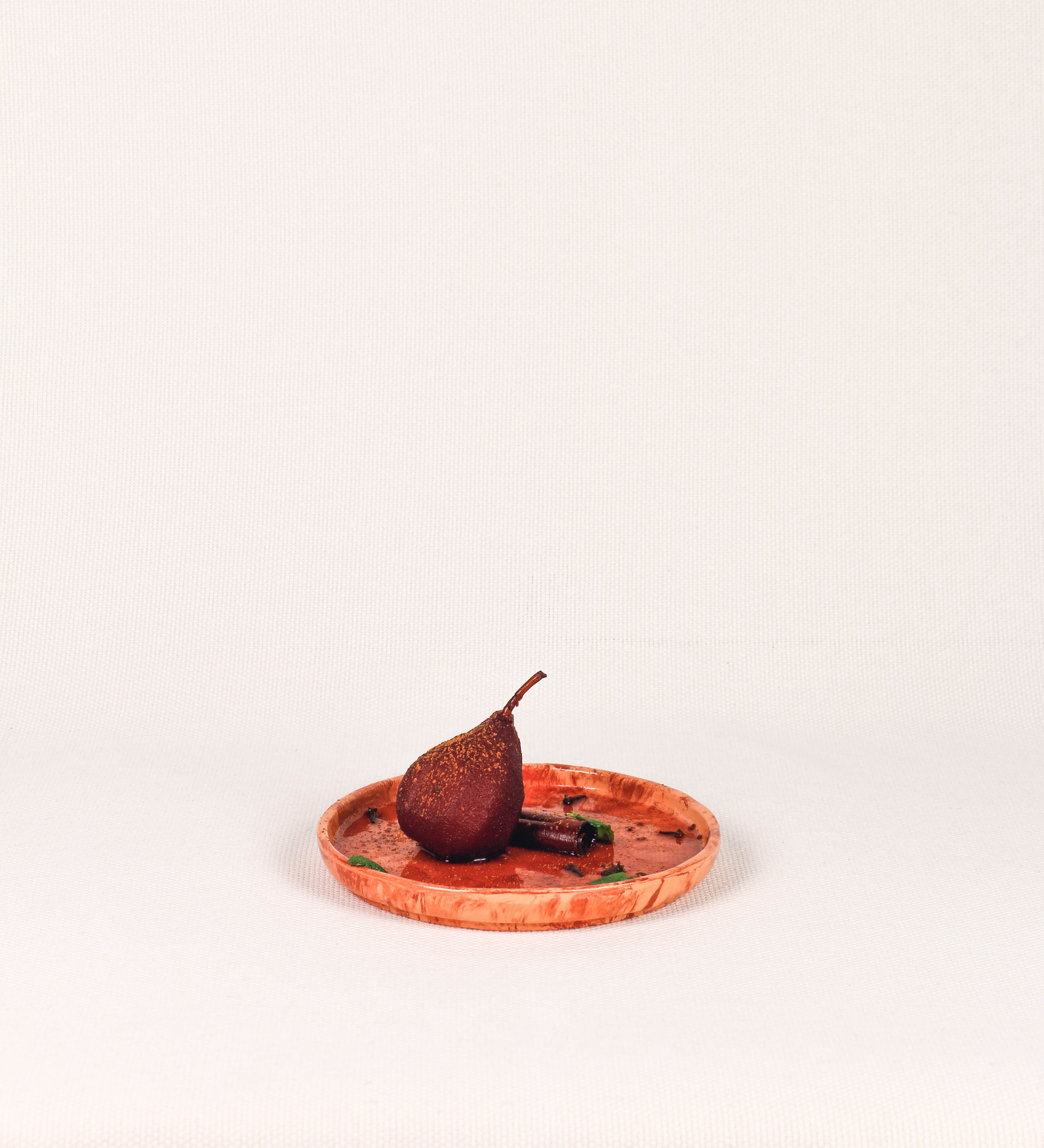 Prato de sobremesa com design minimalista e distinto. O prato é de barro, com uma mistura dois tipos de barro diferentes, um mais escuro e outro mais claro. Esta mistura cria um desenho de formas abstratas e aleatórias, que se espalham por todas as superfícies do prato. Tem um acabamento vidrado transparente com brilho, conferindo um toque de sofisticação e preservando os tons naturais dos barros. A forma do prato é circular, com uma borda envolvente de altura baixa e design simples e minimalista. 