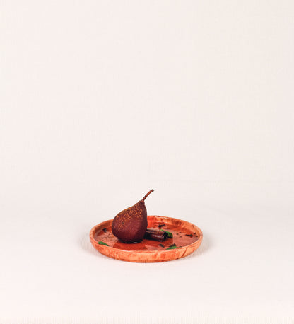 Prato de sobremesa com design minimalista e distinto. O prato é de barro, com uma mistura dois tipos de barro diferentes, um mais escuro e outro mais claro. Esta mistura cria um desenho de formas abstratas e aleatórias, que se espalham por todas as superfícies do prato. Tem um acabamento vidrado transparente com brilho, conferindo um toque de sofisticação e preservando os tons naturais dos barros. A forma do prato é circular, com uma borda envolvente de altura baixa e design simples e minimalista. 