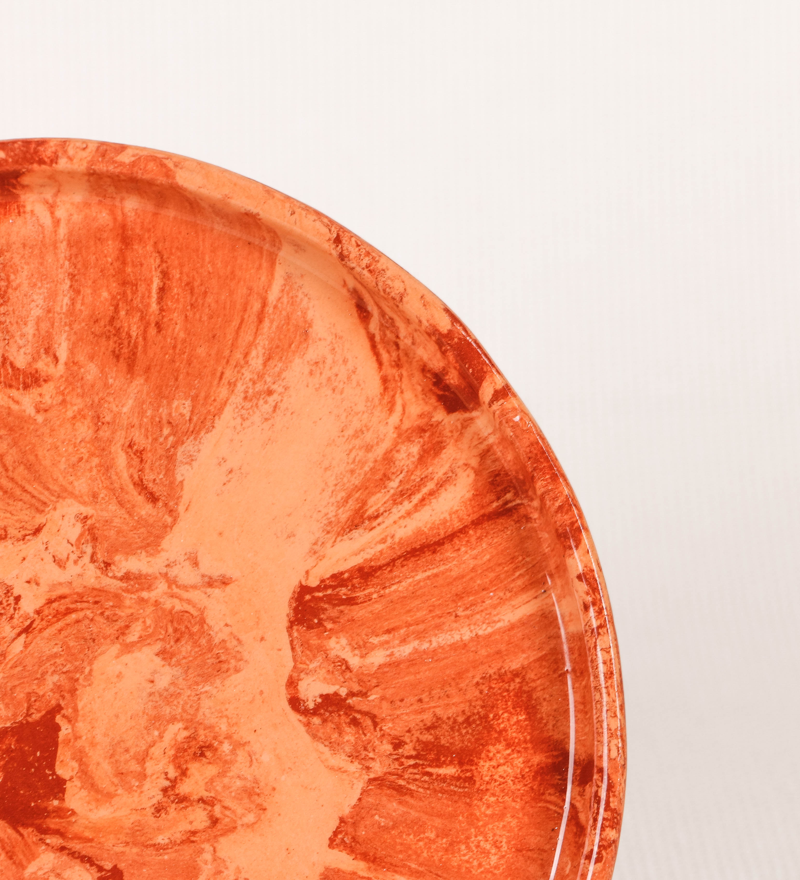 Prato de sobremesa com design minimalista e distinto. O prato é de barro, com uma mistura dois tipos de barro diferentes, um mais escuro e outro mais claro. Esta mistura cria um desenho de formas abstratas e aleatórias, que se espalham por todas as superfícies do prato. Tem um acabamento vidrado transparente com brilho, conferindo um toque de sofisticação e preservando os tons naturais dos barros. A forma do prato é circular, com uma borda envolvente de altura baixa e design simples e minimalista. 