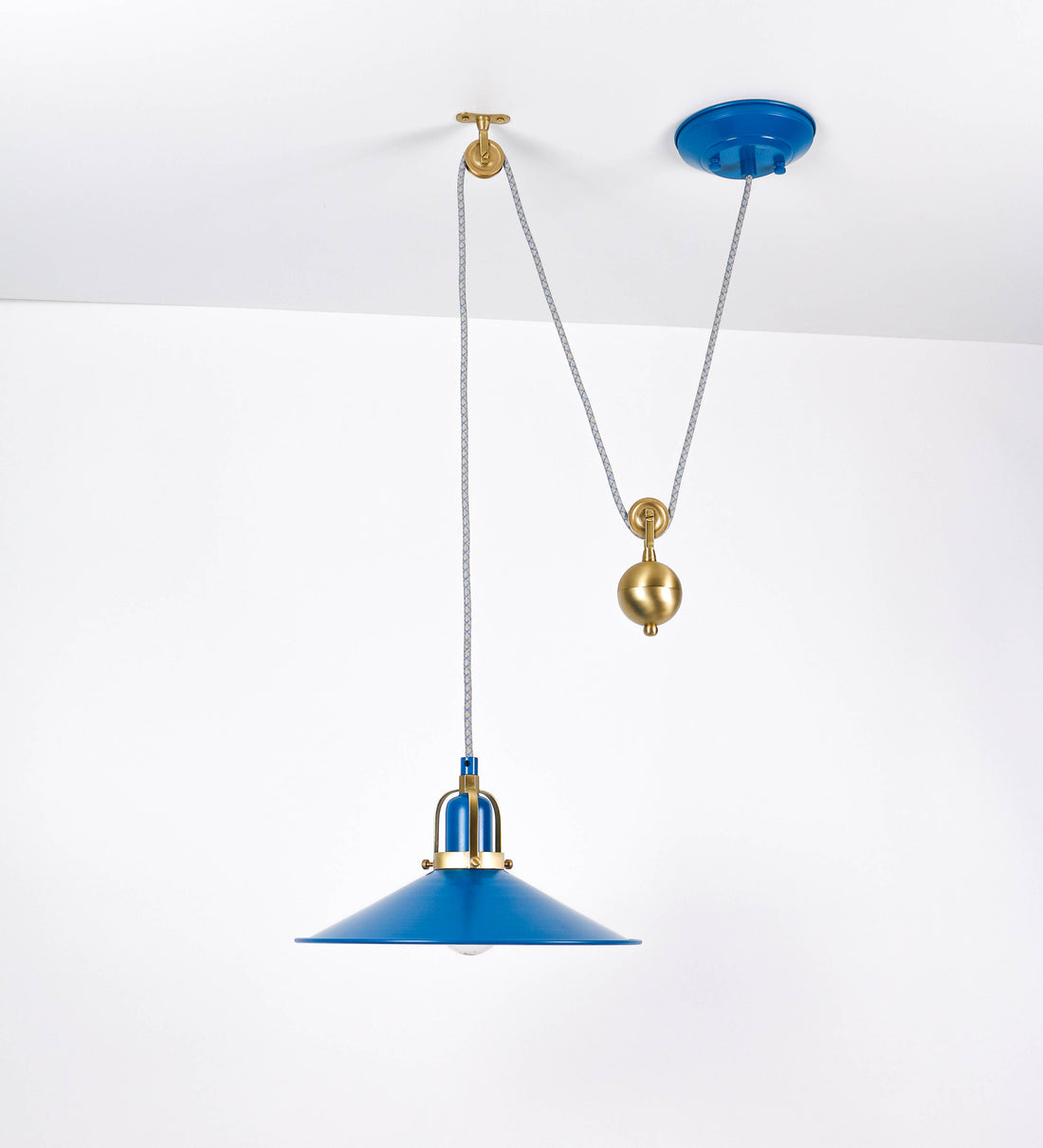 Suspensão de teto composta por uma base circular azul vintage de onde desce um cabo com padrão de linhas azuis e beges. O cabo passa por uma roldana em latão escovado fixa ao teto, e desce até ao chapéu. Entre a base e a roldana o cabo sustenta uma esfera em latão escovado, que atua como um contrapeso, para ajustar a altura. O chapéu, azul vintage, tem formato cónico invertido, uma borda ligeiramente levantada e interior branco. No topo do chapéu há um suporte em latão escovado que conecta o chapéu ao cabo.