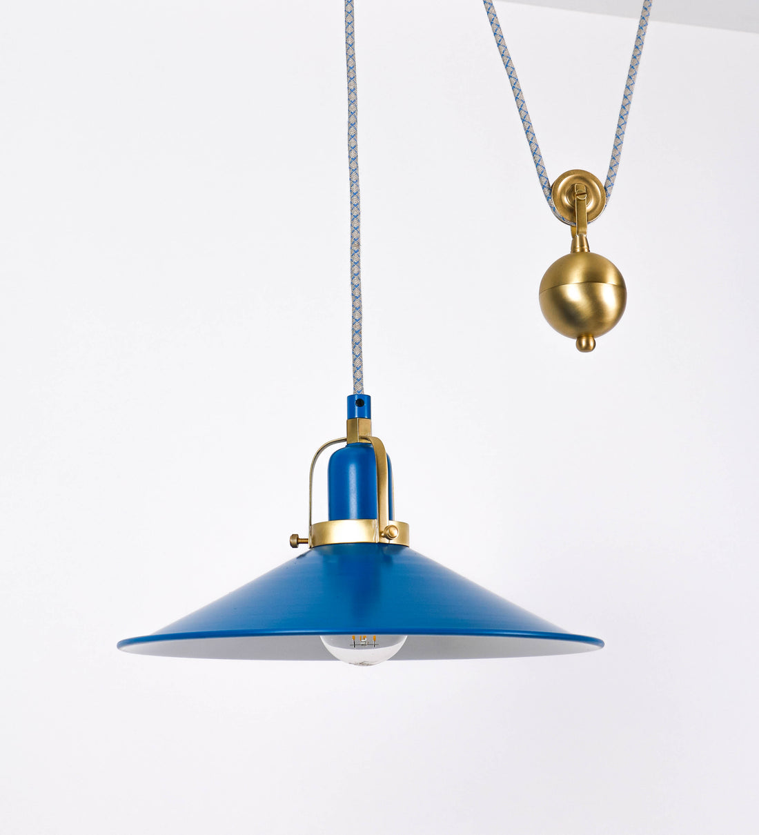 Suspensão de teto composta por uma base circular azul vintage de onde desce um cabo com padrão de linhas azuis e beges. O cabo passa por uma roldana em latão escovado fixa ao teto, e desce até ao chapéu. Entre a base e a roldana o cabo sustenta uma esfera em latão escovado, que atua como um contrapeso, para ajustar a altura. O chapéu, azul vintage, tem formato cónico invertido, uma borda ligeiramente levantada e interior branco. No topo do chapéu há um suporte em latão escovado que conecta o chapéu ao cabo.