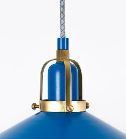 Suspensão de teto composta por uma base circular azul vintage de onde desce um cabo com padrão de linhas azuis e beges. O cabo passa por uma roldana em latão escovado fixa ao teto, e desce até ao chapéu. Entre a base e a roldana o cabo sustenta uma esfera em latão escovado, que atua como um contrapeso, para ajustar a altura. O chapéu, azul vintage, tem formato cónico invertido, uma borda ligeiramente levantada e interior branco. No topo do chapéu há um suporte em latão escovado que conecta o chapéu ao cabo.