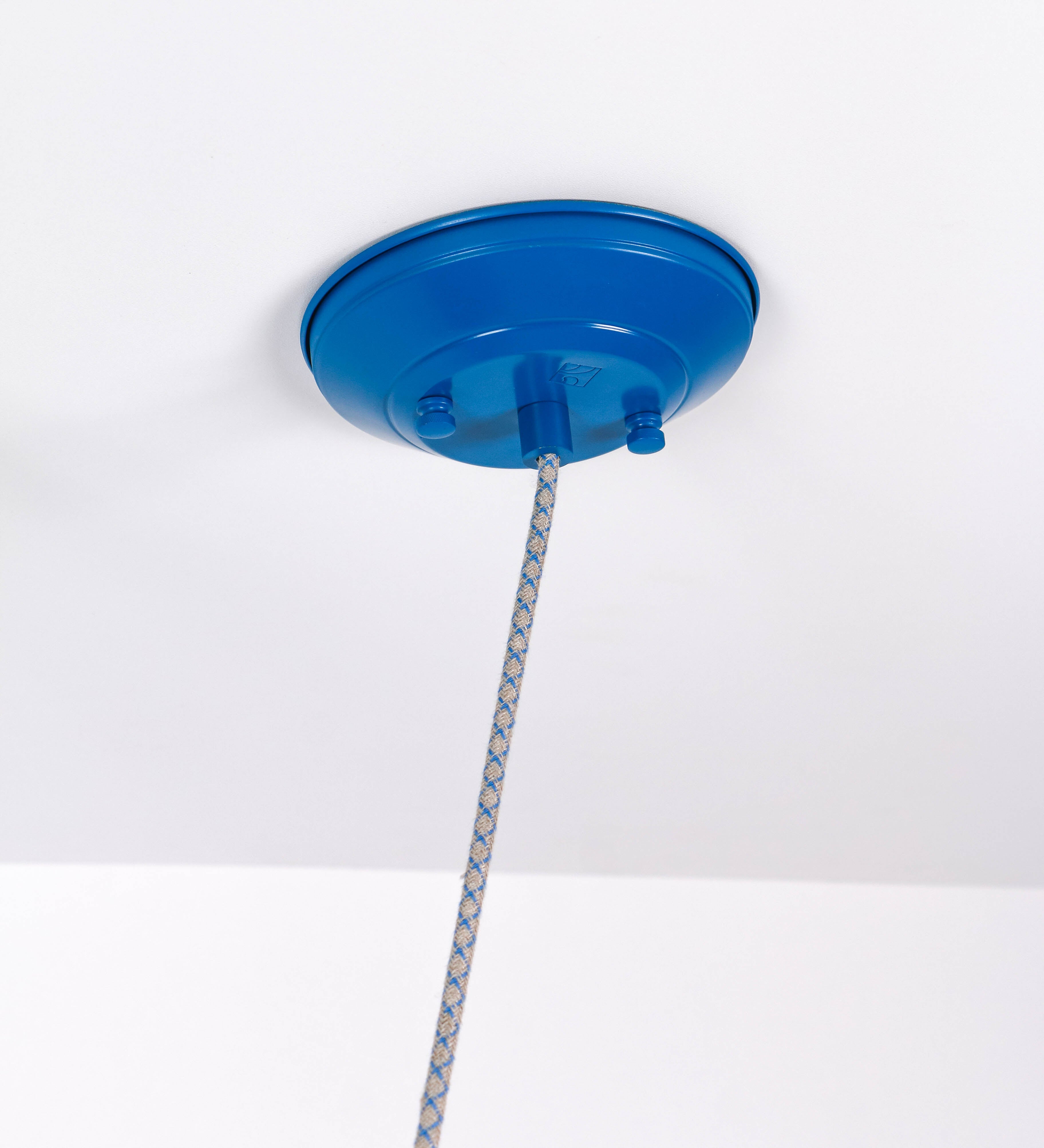Suspensão de teto composta por uma base circular azul vintage de onde desce um cabo com padrão de linhas azuis e beges. O cabo passa por uma roldana em latão escovado fixa ao teto, e desce até ao chapéu. Entre a base e a roldana o cabo sustenta uma esfera em latão escovado, que atua como um contrapeso, para ajustar a altura. O chapéu, azul vintage, tem formato cónico invertido, uma borda ligeiramente levantada e interior branco. No topo do chapéu há um suporte em latão escovado que conecta o chapéu ao cabo.