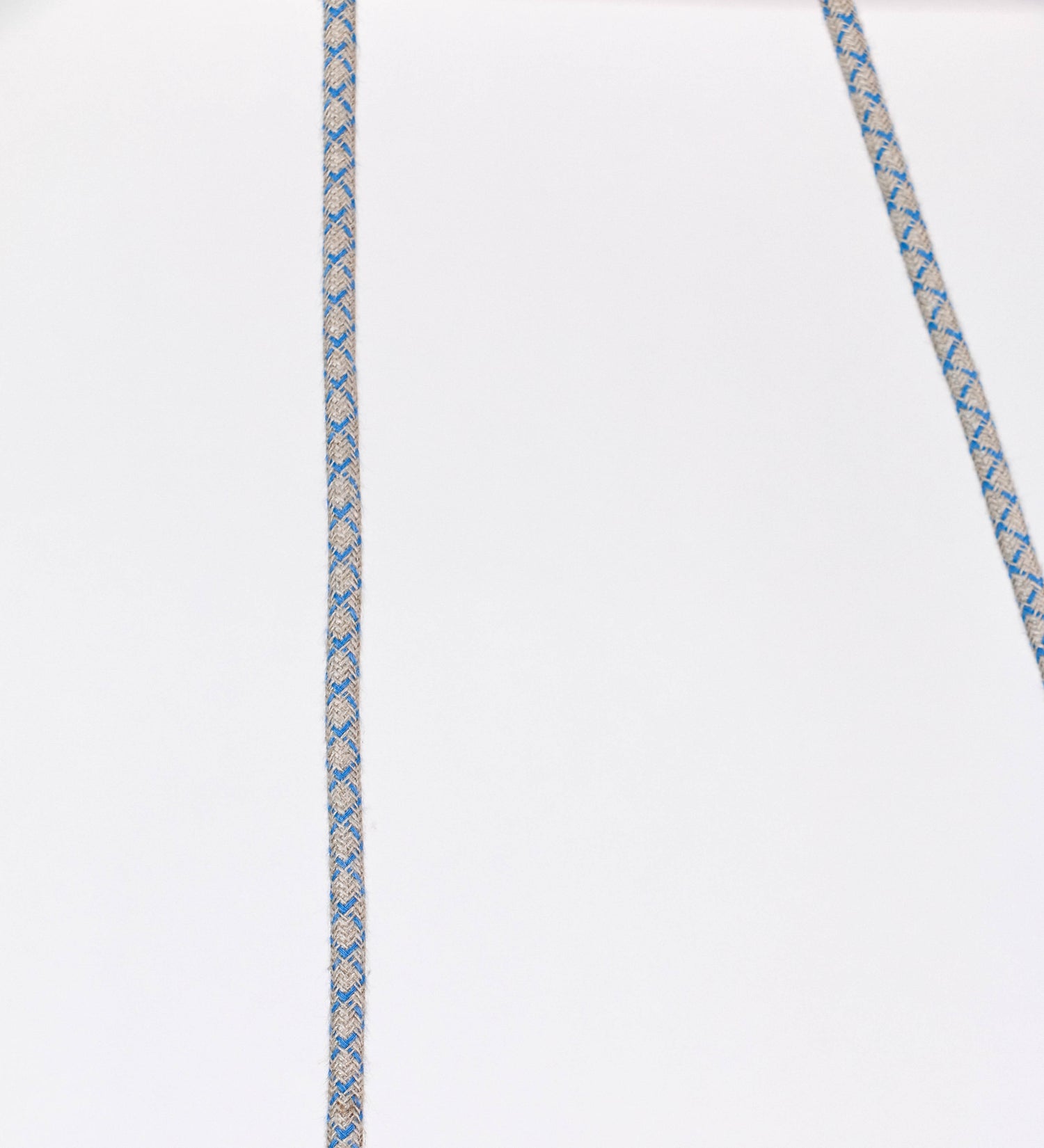 Suspensão de teto composta por uma base circular azul vintage de onde desce um cabo com padrão de linhas azuis e beges. O cabo passa por uma roldana em latão escovado fixa ao teto, e desce até ao chapéu. Entre a base e a roldana o cabo sustenta uma esfera em latão escovado, que atua como um contrapeso, para ajustar a altura. O chapéu, azul vintage, tem formato cónico invertido, uma borda ligeiramente levantada e interior branco. No topo do chapéu há um suporte em latão escovado que conecta o chapéu ao cabo.