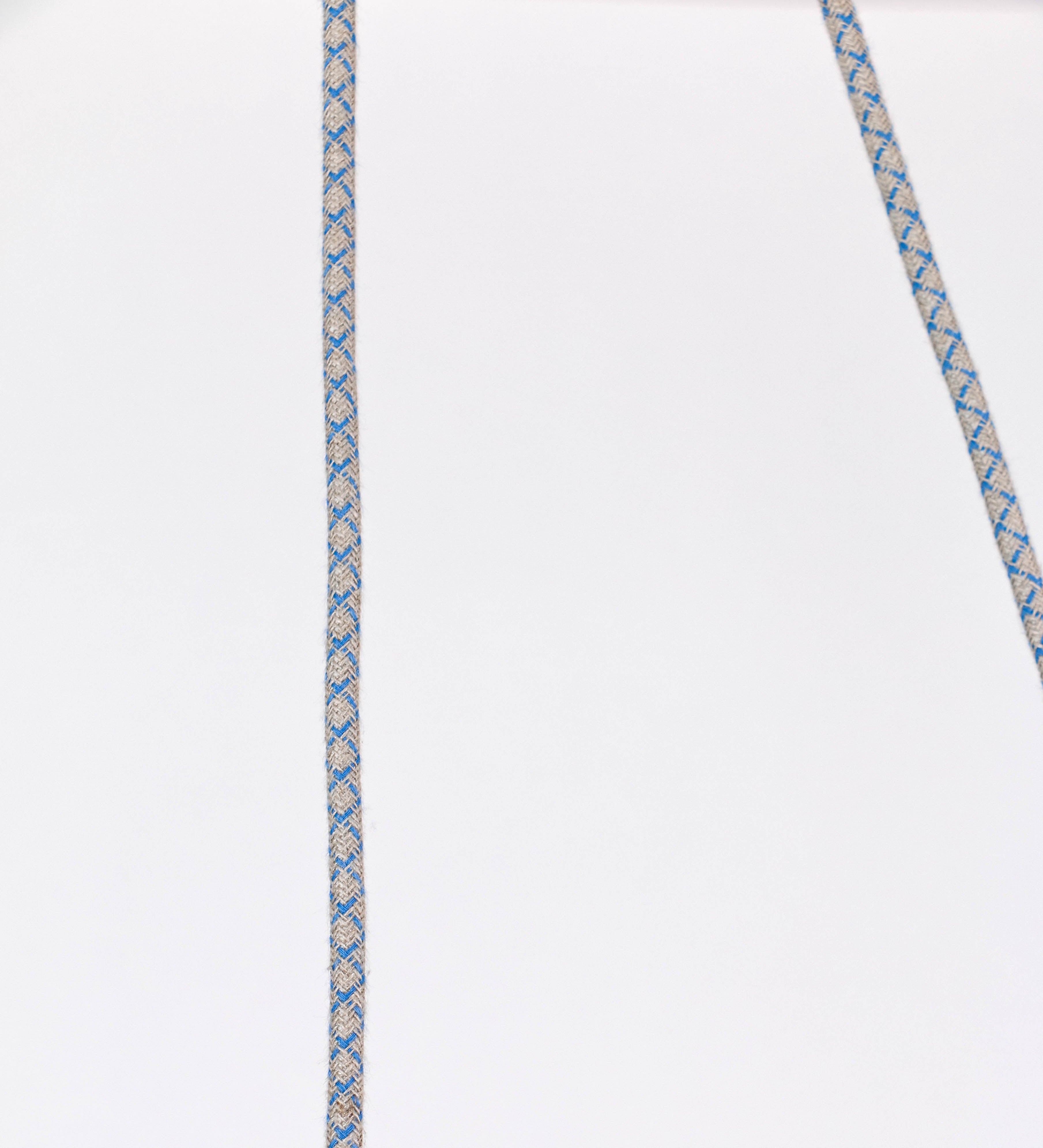 Suspensão de teto composta por uma base circular azul vintage de onde desce um cabo com padrão de linhas azuis e beges. O cabo passa por uma roldana em latão escovado fixa ao teto, e desce até ao chapéu. Entre a base e a roldana o cabo sustenta uma esfera em latão escovado, que atua como um contrapeso, para ajustar a altura. O chapéu, azul vintage, tem formato cónico invertido, uma borda ligeiramente levantada e interior branco. No topo do chapéu há um suporte em latão escovado que conecta o chapéu ao cabo.