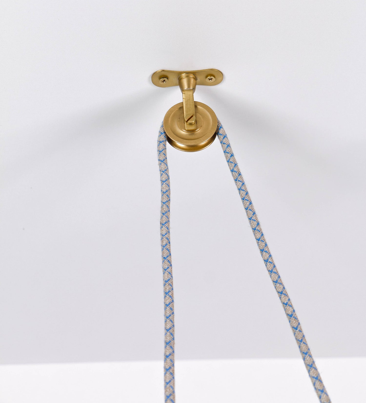 Suspensão de teto composta por uma base circular azul vintage de onde desce um cabo com padrão de linhas azuis e beges. O cabo passa por uma roldana em latão escovado fixa ao teto, e desce até ao chapéu. Entre a base e a roldana o cabo sustenta uma esfera em latão escovado, que atua como um contrapeso, para ajustar a altura. O chapéu, azul vintage, tem formato cónico invertido, uma borda ligeiramente levantada e interior branco. No topo do chapéu há um suporte em latão escovado que conecta o chapéu ao cabo.