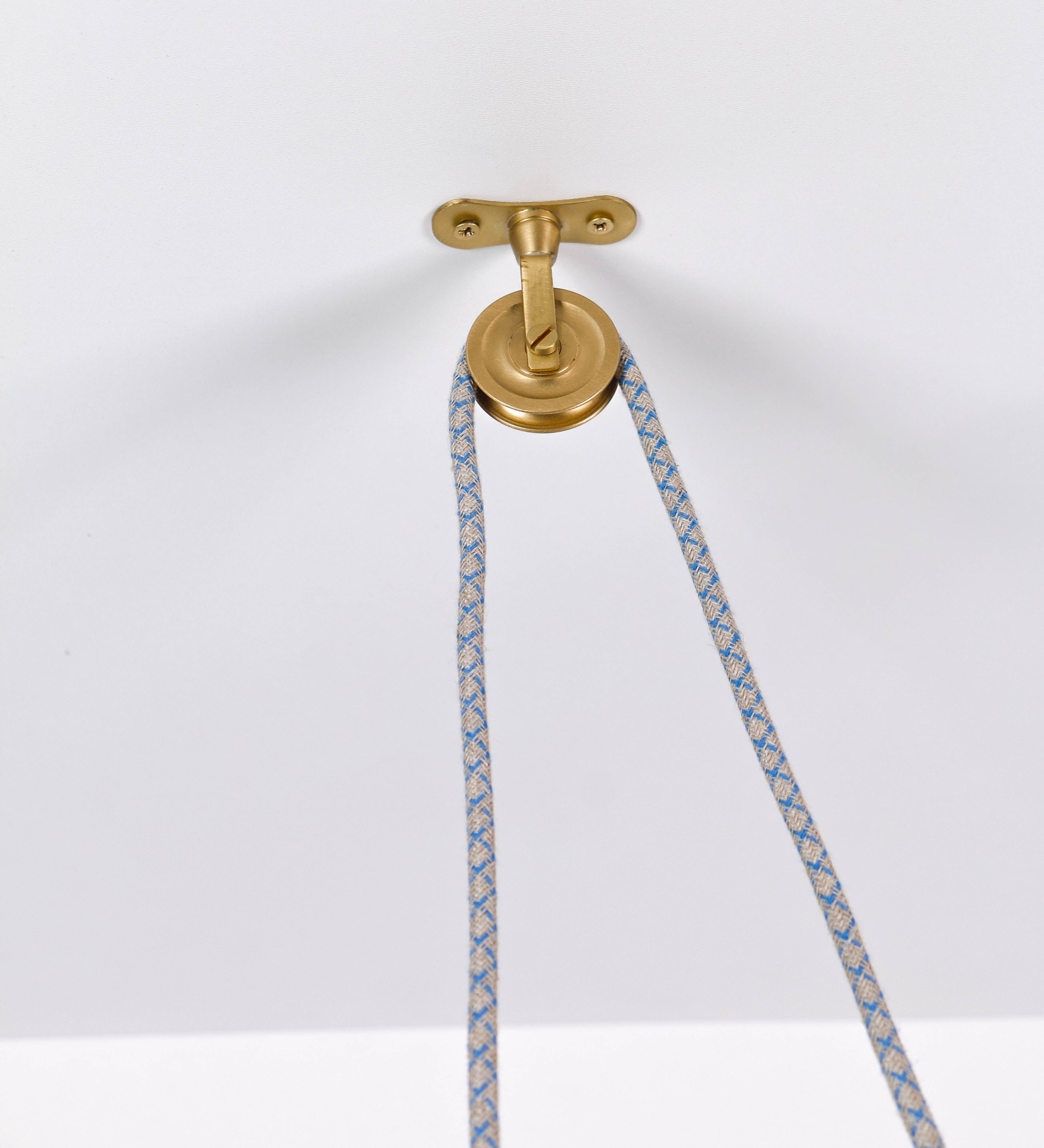 Suspensão de teto composta por uma base circular azul vintage de onde desce um cabo com padrão de linhas azuis e beges. O cabo passa por uma roldana em latão escovado fixa ao teto, e desce até ao chapéu. Entre a base e a roldana o cabo sustenta uma esfera em latão escovado, que atua como um contrapeso, para ajustar a altura. O chapéu, azul vintage, tem formato cónico invertido, uma borda ligeiramente levantada e interior branco. No topo do chapéu há um suporte em latão escovado que conecta o chapéu ao cabo.
