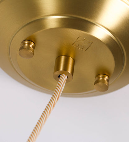 Suspensão de teto em latão escovado, composta por uma base circular, de onde desce um cabo revestido têxtil com um padrão com linhas douradas e brancas. O cabo passa por uma roldana fixa ao teto, e desce até ao chapéu. Entre a base e a roldana, o cabo sustenta uma esfera, que atua como um contrapeso, para ajustar a altura do candeeiro. O chapéu tem formato cónico invertido e uma borda ligeiramente levantada. No topo do chapéu, há um suporte circular com três pequenos braços que conecta o chapéu ao cabo.
