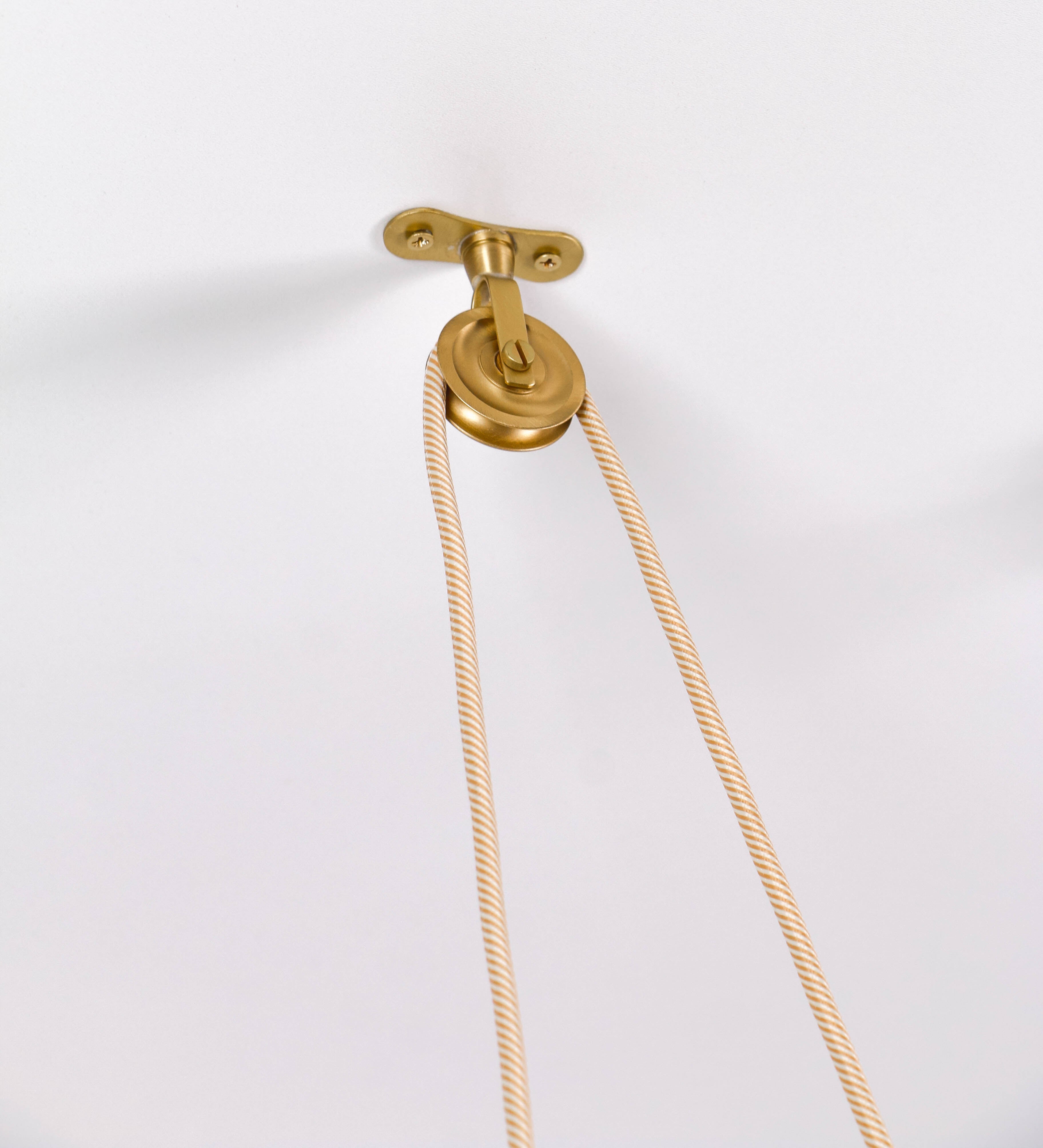Suspensão de teto em latão escovado, composta por uma base circular, de onde desce um cabo revestido têxtil com um padrão com linhas douradas e brancas. O cabo passa por uma roldana fixa ao teto, e desce até ao chapéu. Entre a base e a roldana, o cabo sustenta uma esfera, que atua como um contrapeso, para ajustar a altura do candeeiro. O chapéu tem formato cónico invertido e uma borda ligeiramente levantada. No topo do chapéu, há um suporte circular com três pequenos braços que conecta o chapéu ao cabo.