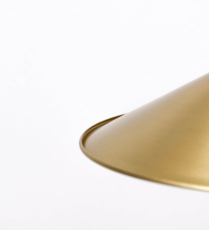 Suspensão de teto em latão escovado, composta por uma base circular, de onde desce um cabo revestido têxtil com um padrão com linhas douradas e brancas. O cabo passa por uma roldana fixa ao teto, e desce até ao chapéu. Entre a base e a roldana, o cabo sustenta uma esfera, que atua como um contrapeso, para ajustar a altura do candeeiro. O chapéu tem formato cónico invertido e uma borda ligeiramente levantada. No topo do chapéu, há um suporte circular com três pequenos braços que conecta o chapéu ao cabo.