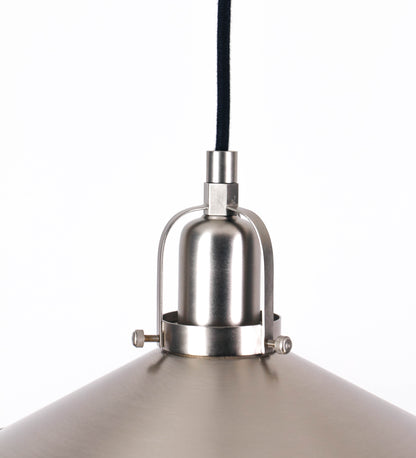 Suspensão de teto em níquel escovado, composta por uma base circular, de onde desce um cabo revestido têxtil preto. O cabo passa por uma roldana fixa ao teto, e desce até ao chapéu. Entre a base e a roldana, o cabo sustenta uma esfera, que atua como um contrapeso, para ajustar a altura do candeeiro. O chapéu tem formato cónico invertido e uma borda ligeiramente levantada. No topo do chapéu, há um suporte circular com três pequenos braços que conecta o chapéu ao cabo.