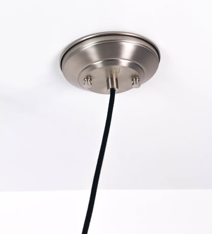 Suspensão de teto em níquel escovado, composta por uma base circular, de onde desce um cabo revestido têxtil preto. O cabo passa por uma roldana fixa ao teto, e desce até ao chapéu. Entre a base e a roldana, o cabo sustenta uma esfera, que atua como um contrapeso, para ajustar a altura do candeeiro. O chapéu tem formato cónico invertido e uma borda ligeiramente levantada. No topo do chapéu, há um suporte circular com três pequenos braços que conecta o chapéu ao cabo.