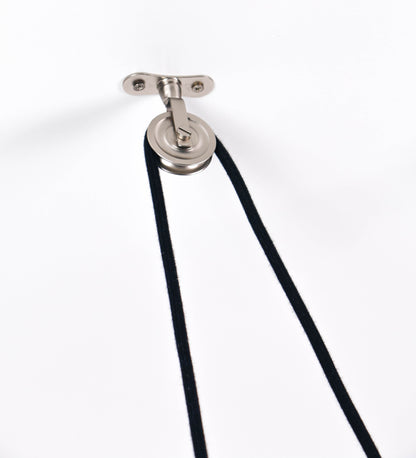 Suspensão de teto em níquel escovado, composta por uma base circular, de onde desce um cabo revestido têxtil preto. O cabo passa por uma roldana fixa ao teto, e desce até ao chapéu. Entre a base e a roldana, o cabo sustenta uma esfera, que atua como um contrapeso, para ajustar a altura do candeeiro. O chapéu tem formato cónico invertido e uma borda ligeiramente levantada. No topo do chapéu, há um suporte circular com três pequenos braços que conecta o chapéu ao cabo.