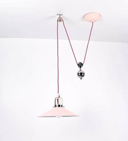 Suspensão de teto composta por uma base circular rosa clara, de onde desce um cabo revestido têxtil rosa velho. O cabo passa por uma roldana em níquel polido, fixa ao teto, e desce até ao chapéu. Entre a base e a roldana, o cabo sustenta uma esfera, em níquel polido, que atua como um contrapeso, para ajustar a altura. O chapéu, rosa claro, tem formato cónico invertido, uma borda ligeiramente levantada e interior branco. No topo do chapéu, há um suporte em níquel polido que conecta o chapéu ao cabo.