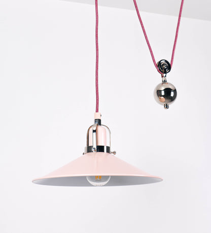 Suspensão de teto composta por uma base circular rosa clara, de onde desce um cabo revestido têxtil rosa velho. O cabo passa por uma roldana em níquel polido, fixa ao teto, e desce até ao chapéu. Entre a base e a roldana, o cabo sustenta uma esfera, em níquel polido, que atua como um contrapeso, para ajustar a altura. O chapéu, rosa claro, tem formato cónico invertido, uma borda ligeiramente levantada e interior branco. No topo do chapéu, há um suporte em níquel polido que conecta o chapéu ao cabo.