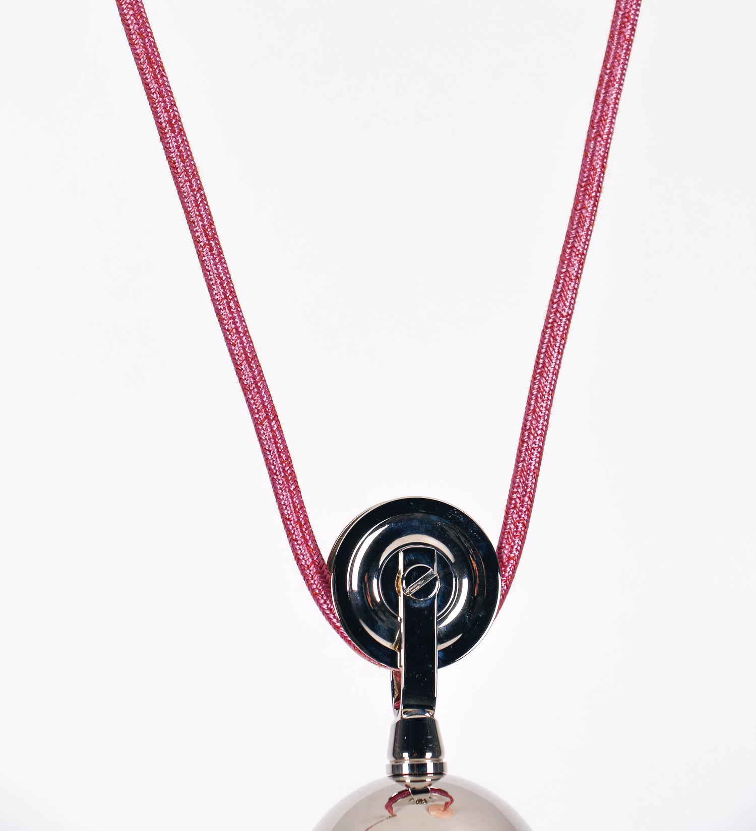 Suspensão de teto composta por uma base circular rosa clara, de onde desce um cabo revestido têxtil rosa velho. O cabo passa por uma roldana em níquel polido, fixa ao teto, e desce até ao chapéu. Entre a base e a roldana, o cabo sustenta uma esfera, em níquel polido, que atua como um contrapeso, para ajustar a altura. O chapéu, rosa claro, tem formato cónico invertido, uma borda ligeiramente levantada e interior branco. No topo do chapéu, há um suporte em níquel polido que conecta o chapéu ao cabo.