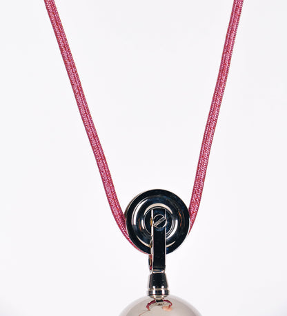 Suspensão de teto composta por uma base circular rosa clara, de onde desce um cabo revestido têxtil rosa velho. O cabo passa por uma roldana em níquel polido, fixa ao teto, e desce até ao chapéu. Entre a base e a roldana, o cabo sustenta uma esfera, em níquel polido, que atua como um contrapeso, para ajustar a altura. O chapéu, rosa claro, tem formato cónico invertido, uma borda ligeiramente levantada e interior branco. No topo do chapéu, há um suporte em níquel polido que conecta o chapéu ao cabo.