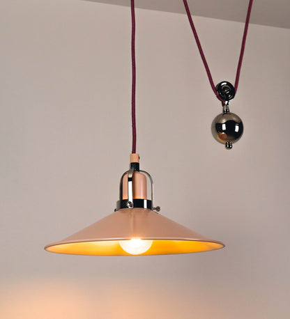 Suspensão de teto composta por uma base circular rosa clara, de onde desce um cabo revestido têxtil rosa velho. O cabo passa por uma roldana em níquel polido, fixa ao teto, e desce até ao chapéu. Entre a base e a roldana, o cabo sustenta uma esfera, em níquel polido, que atua como um contrapeso, para ajustar a altura. O chapéu, rosa claro, tem formato cónico invertido, uma borda ligeiramente levantada e interior branco. No topo do chapéu, há um suporte em níquel polido que conecta o chapéu ao cabo.