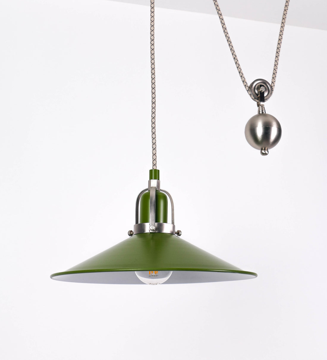 Suspensão de teto composta por uma base circular verde couve-de-bruxelas de onde desce um cabo com padrão de linhas castanhas e beges. O cabo passa por uma roldana em níquel escovado fixa ao teto, e desce até ao chapéu. Entre a base e a roldana o cabo sustenta uma esfera em níquel escovado, que atua como um contrapeso, para ajustar a altura. O chapéu é verde, de formato cónico invertido, uma borda levantada e interior branco. No topo do chapéu há um suporte em níquel escovado que conecta o chapéu ao cabo.