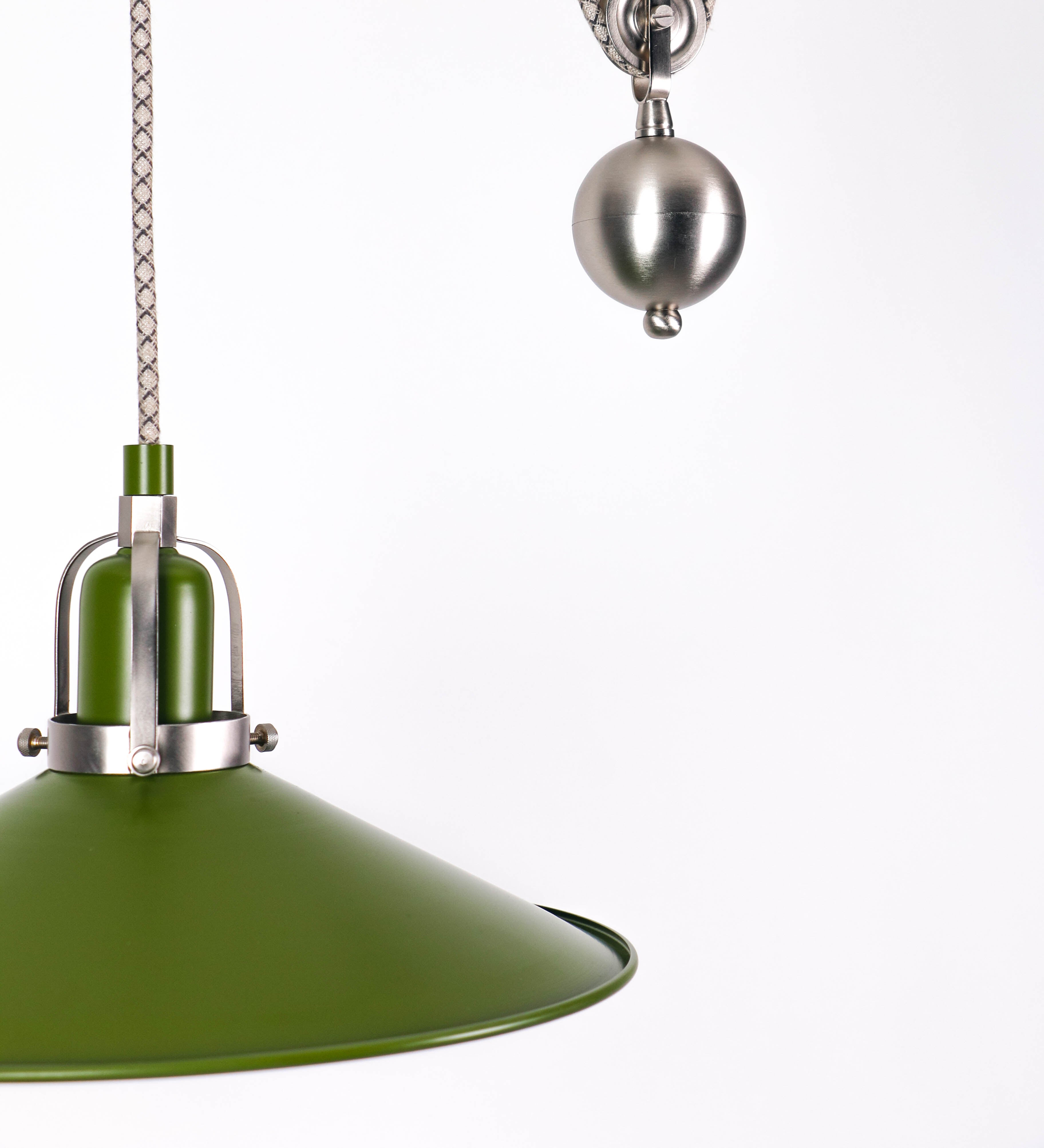 Suspensão de teto composta por uma base circular verde couve-de-bruxelas de onde desce um cabo com padrão de linhas castanhas e beges. O cabo passa por uma roldana em níquel escovado fixa ao teto, e desce até ao chapéu. Entre a base e a roldana o cabo sustenta uma esfera em níquel escovado, que atua como um contrapeso, para ajustar a altura. O chapéu é verde, de formato cónico invertido, uma borda levantada e interior branco. No topo do chapéu há um suporte em níquel escovado que conecta o chapéu ao cabo.