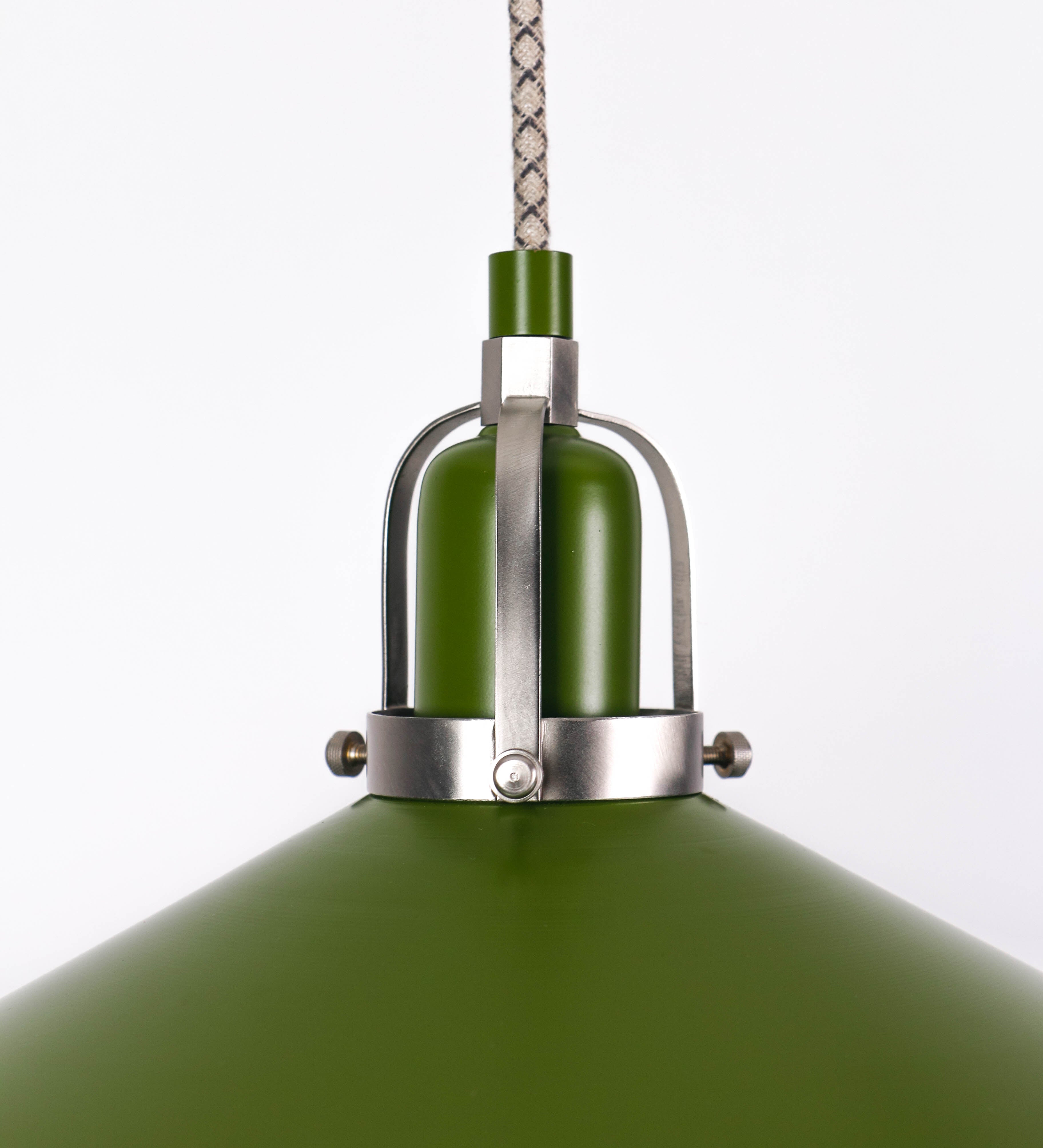 Suspensão de teto composta por uma base circular verde couve-de-bruxelas de onde desce um cabo com padrão de linhas castanhas e beges. O cabo passa por uma roldana em níquel escovado fixa ao teto, e desce até ao chapéu. Entre a base e a roldana o cabo sustenta uma esfera em níquel escovado, que atua como um contrapeso, para ajustar a altura. O chapéu é verde, de formato cónico invertido, uma borda levantada e interior branco. No topo do chapéu há um suporte em níquel escovado que conecta o chapéu ao cabo.