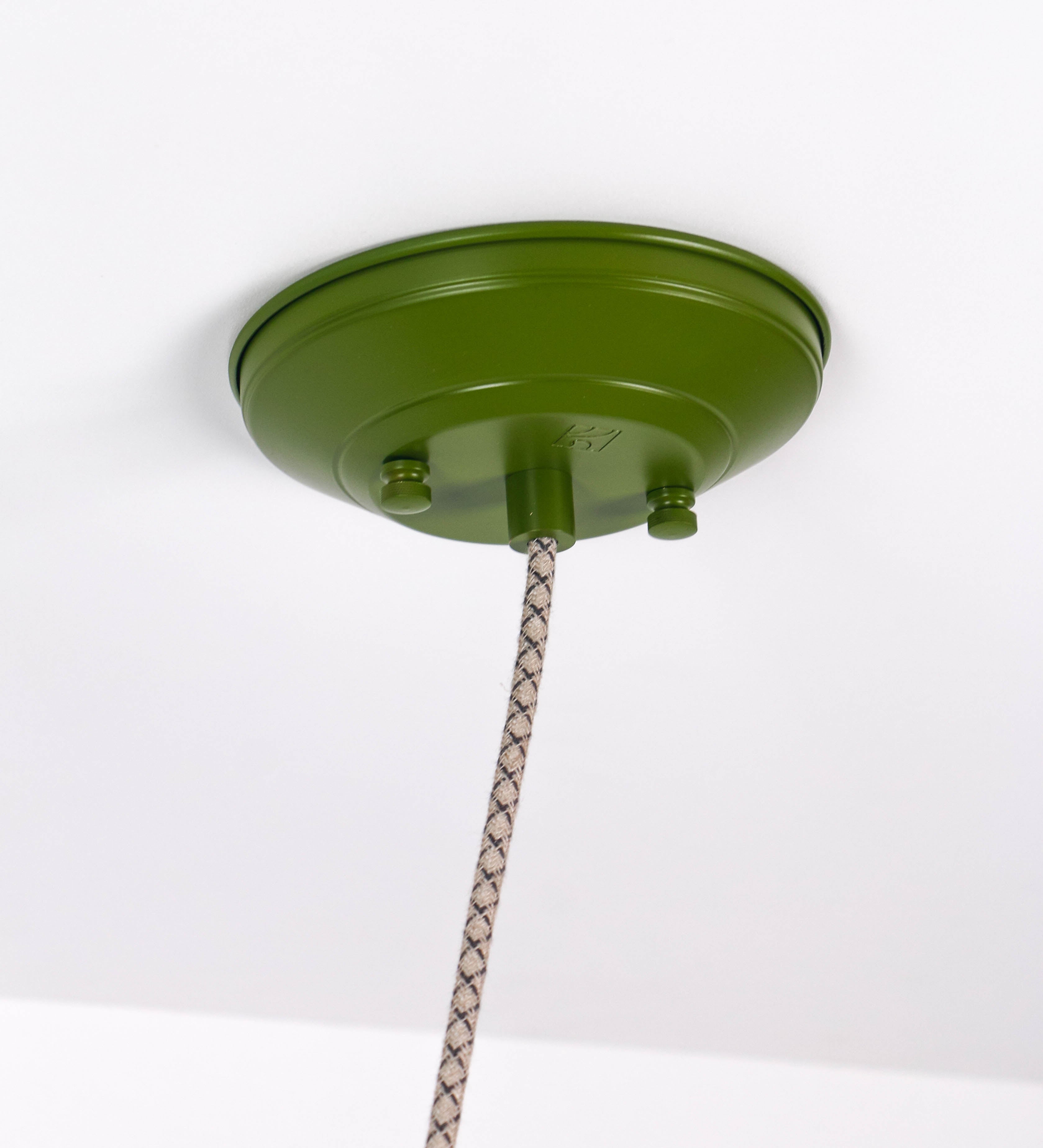 Suspensão de teto composta por uma base circular verde couve-de-bruxelas de onde desce um cabo com padrão de linhas castanhas e beges. O cabo passa por uma roldana em níquel escovado fixa ao teto, e desce até ao chapéu. Entre a base e a roldana o cabo sustenta uma esfera em níquel escovado, que atua como um contrapeso, para ajustar a altura. O chapéu é verde, de formato cónico invertido, uma borda levantada e interior branco. No topo do chapéu há um suporte em níquel escovado que conecta o chapéu ao cabo.