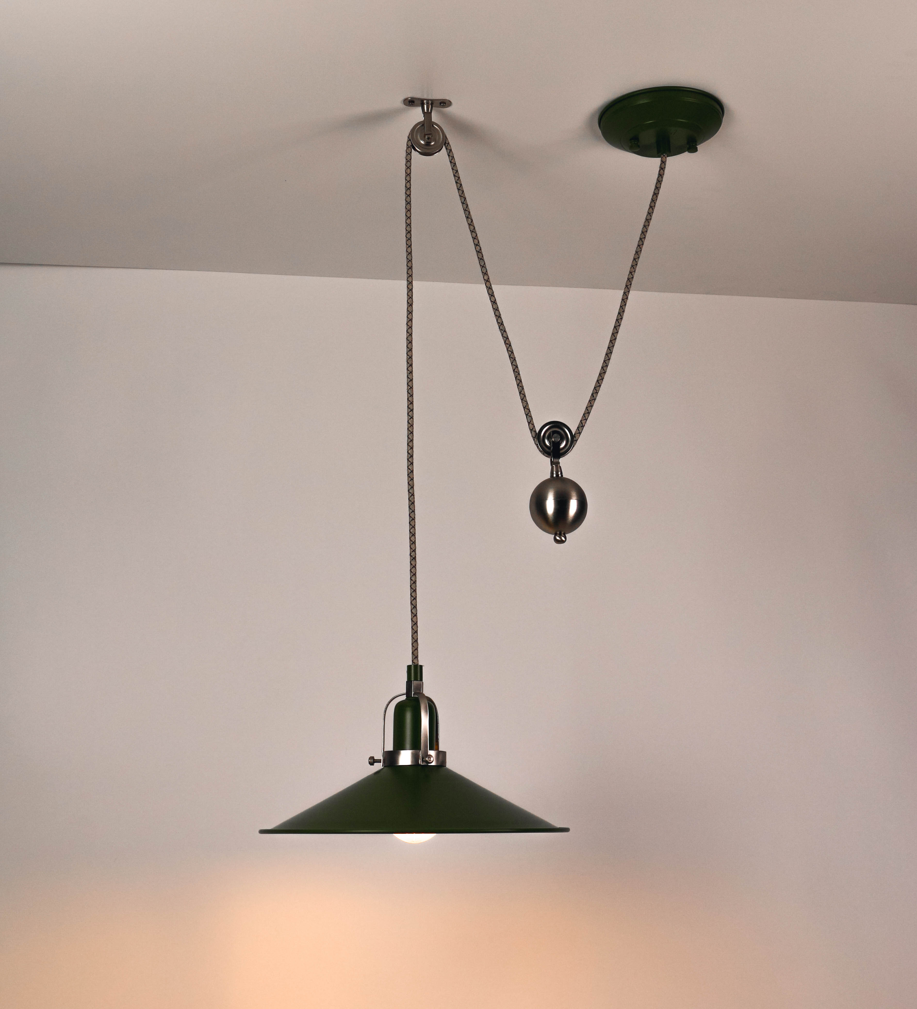 Suspensão de teto composta por uma base circular verde couve-de-bruxelas de onde desce um cabo com padrão de linhas castanhas e beges. O cabo passa por uma roldana em níquel escovado fixa ao teto, e desce até ao chapéu. Entre a base e a roldana o cabo sustenta uma esfera em níquel escovado, que atua como um contrapeso, para ajustar a altura. O chapéu é verde, de formato cónico invertido, uma borda levantada e interior branco. No topo do chapéu há um suporte em níquel escovado que conecta o chapéu ao cabo.