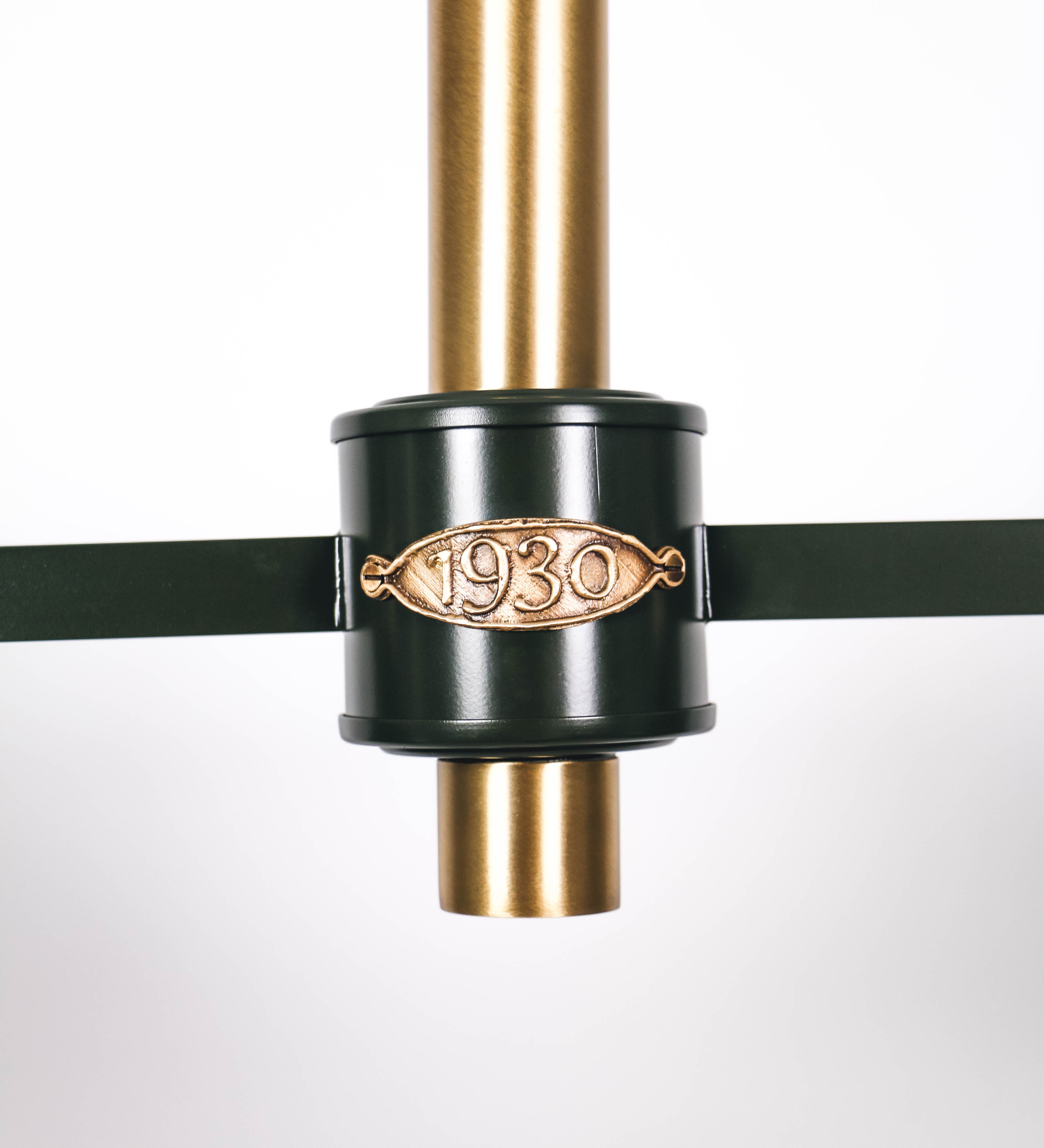 Suspensão de teto moderna e sofisticada. A suspensão é composta por uma base retangular em ouro velho, de onde desce um tubo cilíndrico até a estrutura principal e permite ajustar a altura da suspensão. A estrutura principal é composta por uma barra horizontal verde-azeitona, que sustenta nas extremidades dois chapéus cónicos invertidos no mesmo tom, com interior em ouro velho. No centro da barra horizontal está uma pequena placa oval, em ouro velho, com o ano 1930 inscrito em relevo.