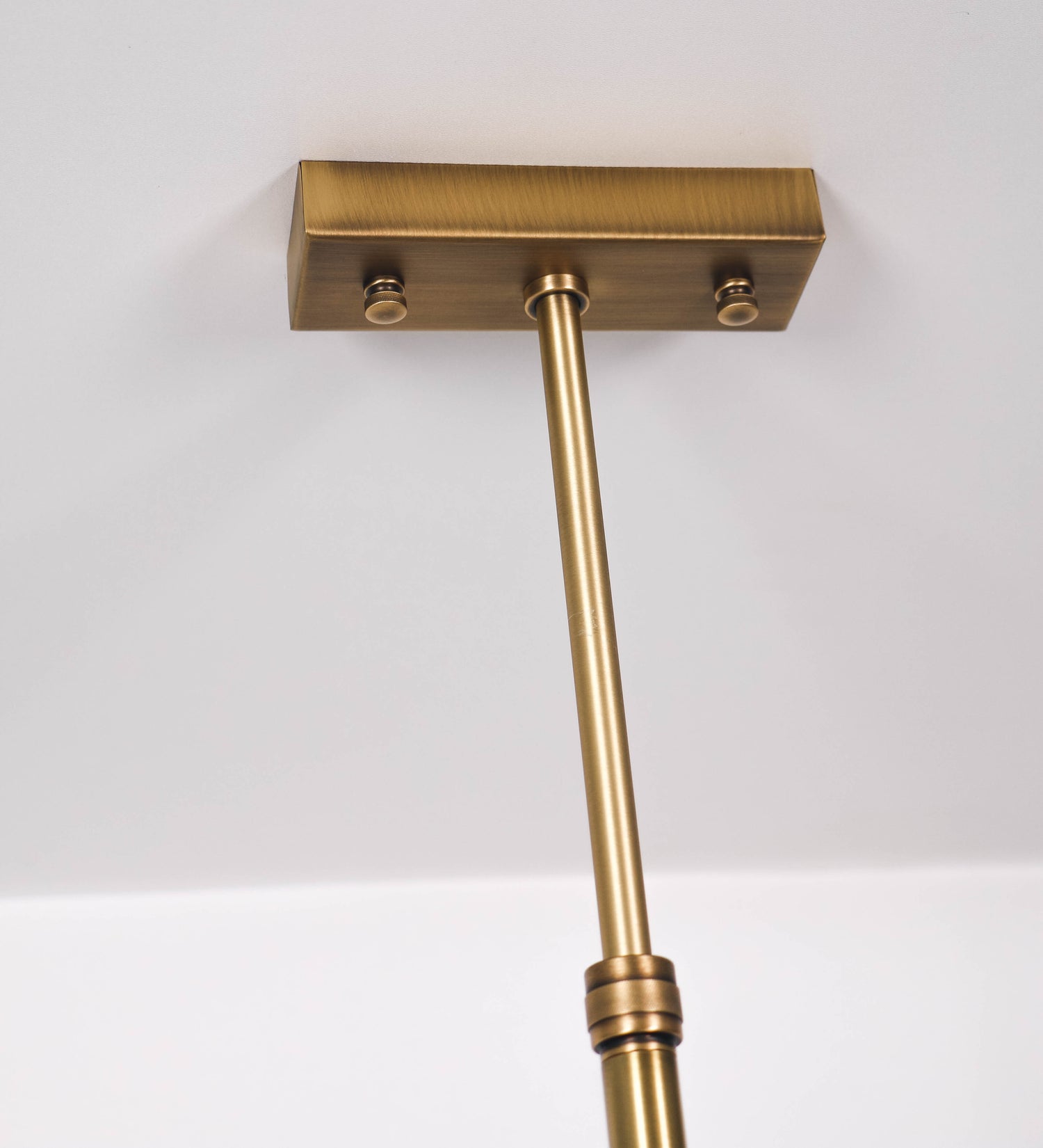 Suspensão de teto moderna e sofisticada. A suspensão é composta por uma base retangular em ouro velho, de onde desce um tubo cilíndrico até a estrutura principal e permite ajustar a altura da suspensão. A estrutura principal é composta por uma barra horizontal verde-azeitona, que sustenta nas extremidades dois chapéus cónicos invertidos no mesmo tom, com interior em ouro velho. No centro da barra horizontal está uma pequena placa oval, em ouro velho, com o ano 1930 inscrito em relevo.